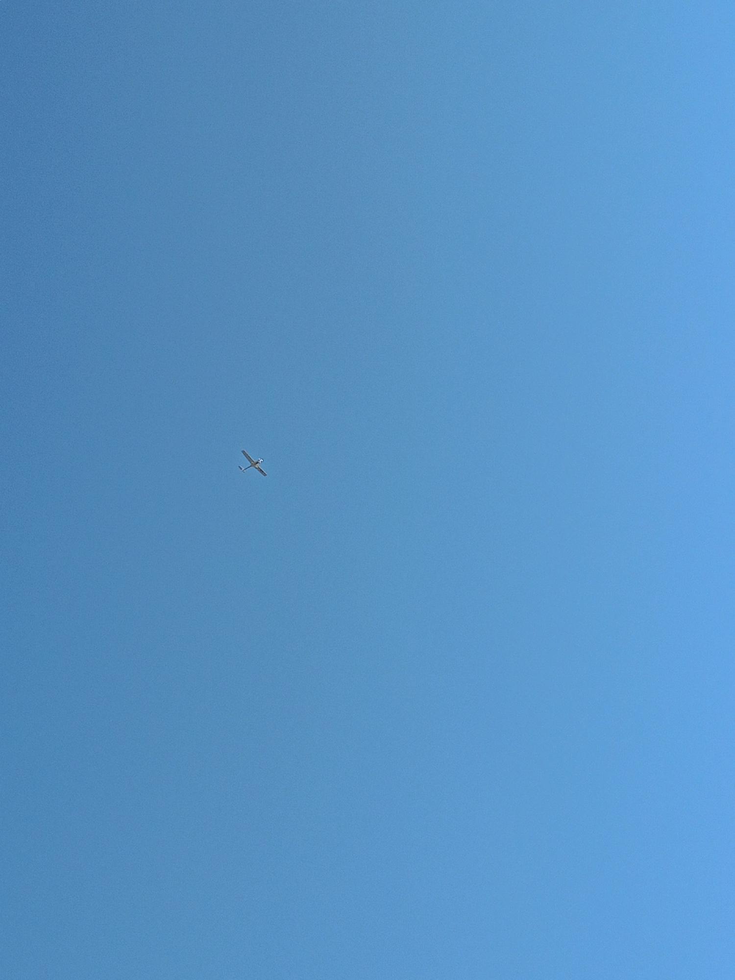 A single, small, white airplane with its wings extended is visible against a clear, bright blue sky. The airplane is positioned in the upper left quadrant of the image and appears to be in flight. There are no other objects or features visible in the image. The scene is devoid of any specific context or identifiable landmarks, making it impossible to determine its location within Peetri alevik, Estonia, or any other geographical area. The image is a straightforward depiction of an airplane in flight against a cloudless sky.