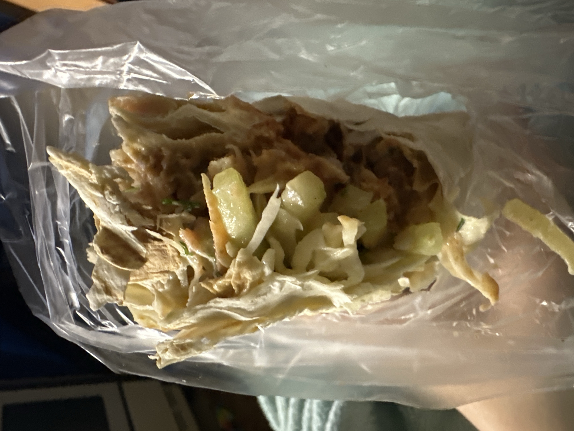 A shawarma wrapped in a clear plastic bag. It contains meat, cabbage, and other ingredients. The location is unknown; there is no indication it is in Moscow, Russia.