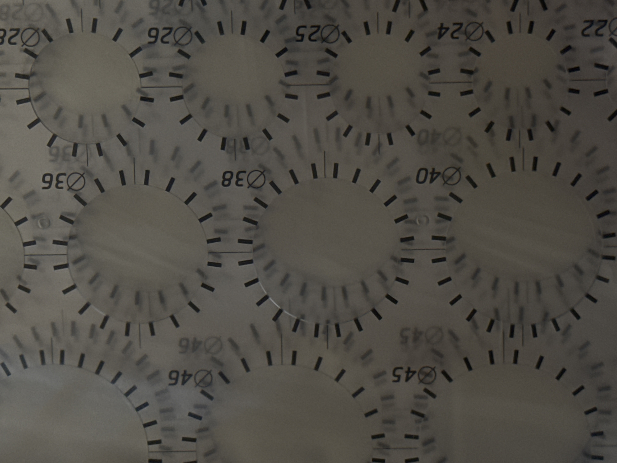 This media file is a close-up, overhead view of a gauge or dial with multiple concentric circles and tick marks. The background appears to be a smooth, reflective surface, possibly metal or plastic, with subtle light reflections and shadows.
The main subjects are the circular gauges themselves, which are marked with numbers and radial lines. The numbers appear to be measurements, with some indicating diameters (indicated by a circle with a line through it, e.g., Ø28, Ø26, Ø25, Ø24, Ø22, Ø40, Ø45, Ø46, Ø36, Ø38). The numbers are printed in a dark, bold font and some are oriented upside down, suggesting a rotational or mirrored layout. The tick marks are short, dark dashes arranged radially around the center of each circle.
There is no discernible activity or event taking place, as the image is static. The lighting is diffused and even, with no indication of a specific time of day or weather conditions. The location context is given as Moscow, Russia, but there are no visual cues within the image to confirm this. The overall impression is one of a technical or industrial object, possibly a measurement tool or part of a larger machine. The reflective surface and sharp details suggest a clean, possibly manufactured environment.