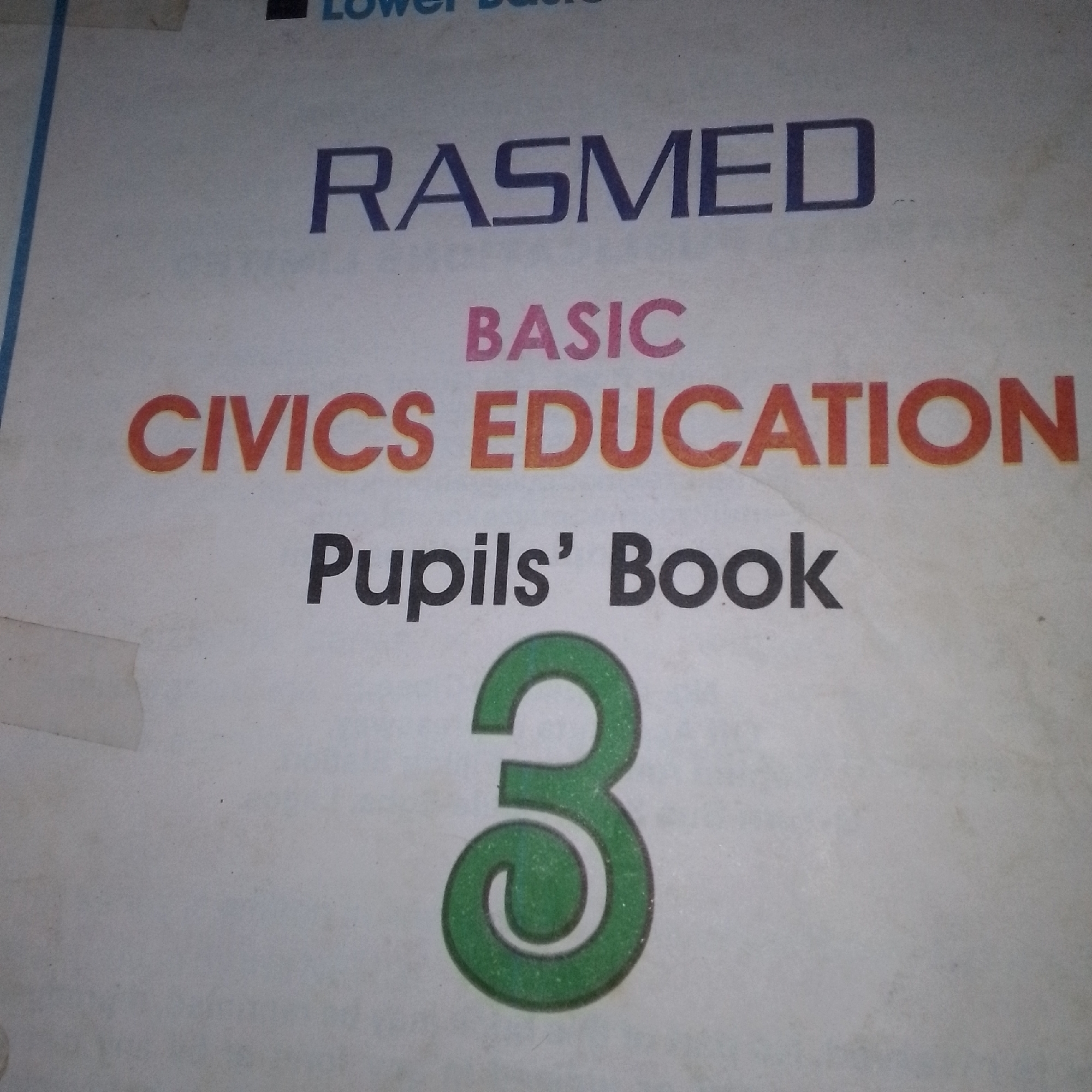 The image shows the cover of a textbook. The title of the book is "RASMED BASIC CIVICS EDUCATION Pupils' Book 3". The text is in a combination of blue, pink, and orange. The number "3" is prominently displayed in green at the bottom of the image. The background is a light-colored, slightly textured paper, possibly a page from a book or pamphlet. There are some minor smudges and imperfections on the surface. The location is not specified in the image.