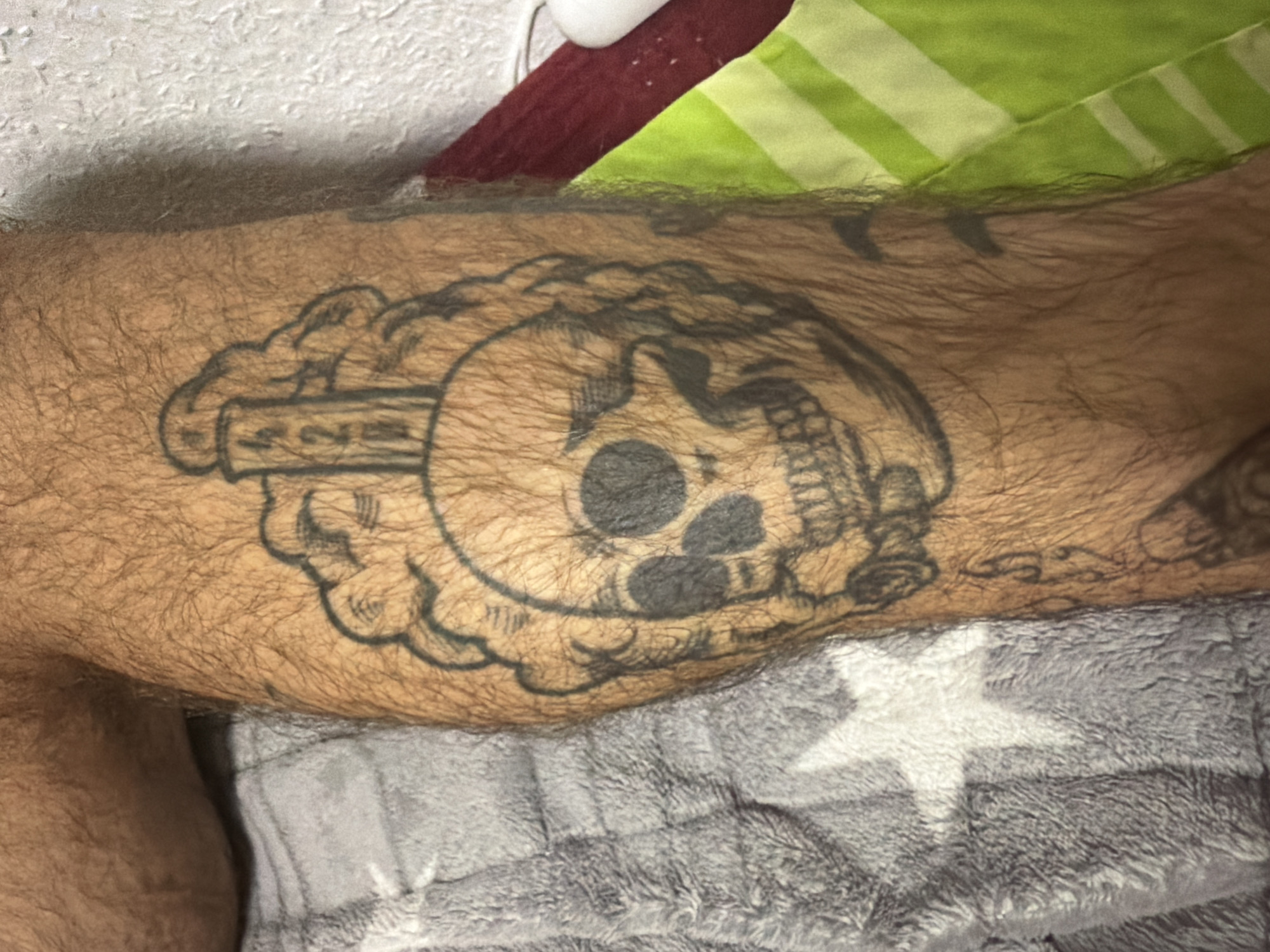 A tattoo of a skull with smoke or clouds around it is visible on a hairy leg. Above the skull, a pillar or monument with the numbers "420" is depicted. The leg is resting on a gray blanket with a white star pattern, and to the right, a green and white striped fabric is visible. The background is a textured white wall. The location is specified as Dorsten, Germany.