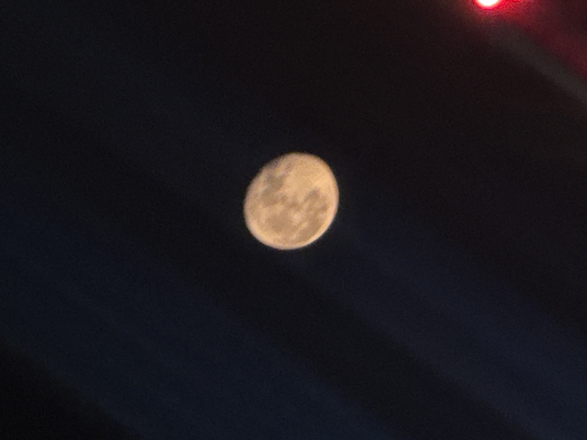 The image shows the moon against a dark blue sky. There is a red light source in the upper right corner. The location is not discernible from the image and therefore cannot be identified as Moscow, Russia.