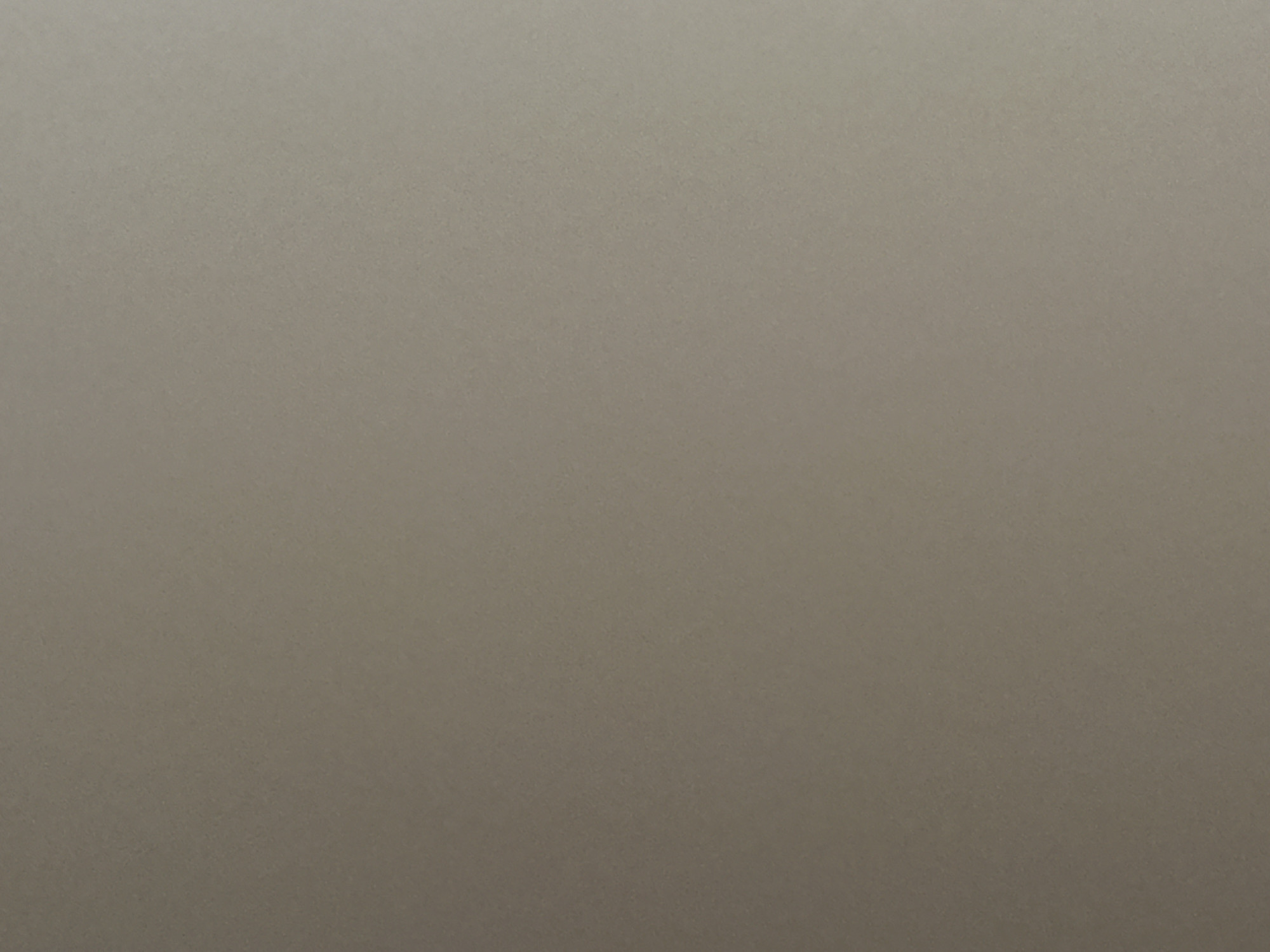The image is a close-up, abstract shot of a textured surface, likely a wall or fabric, in a neutral, earthy tone. There are no discernible objects, people, or actions within the frame. The lighting creates a subtle gradient, with a slightly brighter area towards the top and a darker area towards the bottom, suggesting a diffuse light source from above or the side. The texture appears to be granular or slightly uneven. Without any contextual clues within the image itself, it is impossible to determine its location within the city of Belgrade, Serbia, or any other specific location.