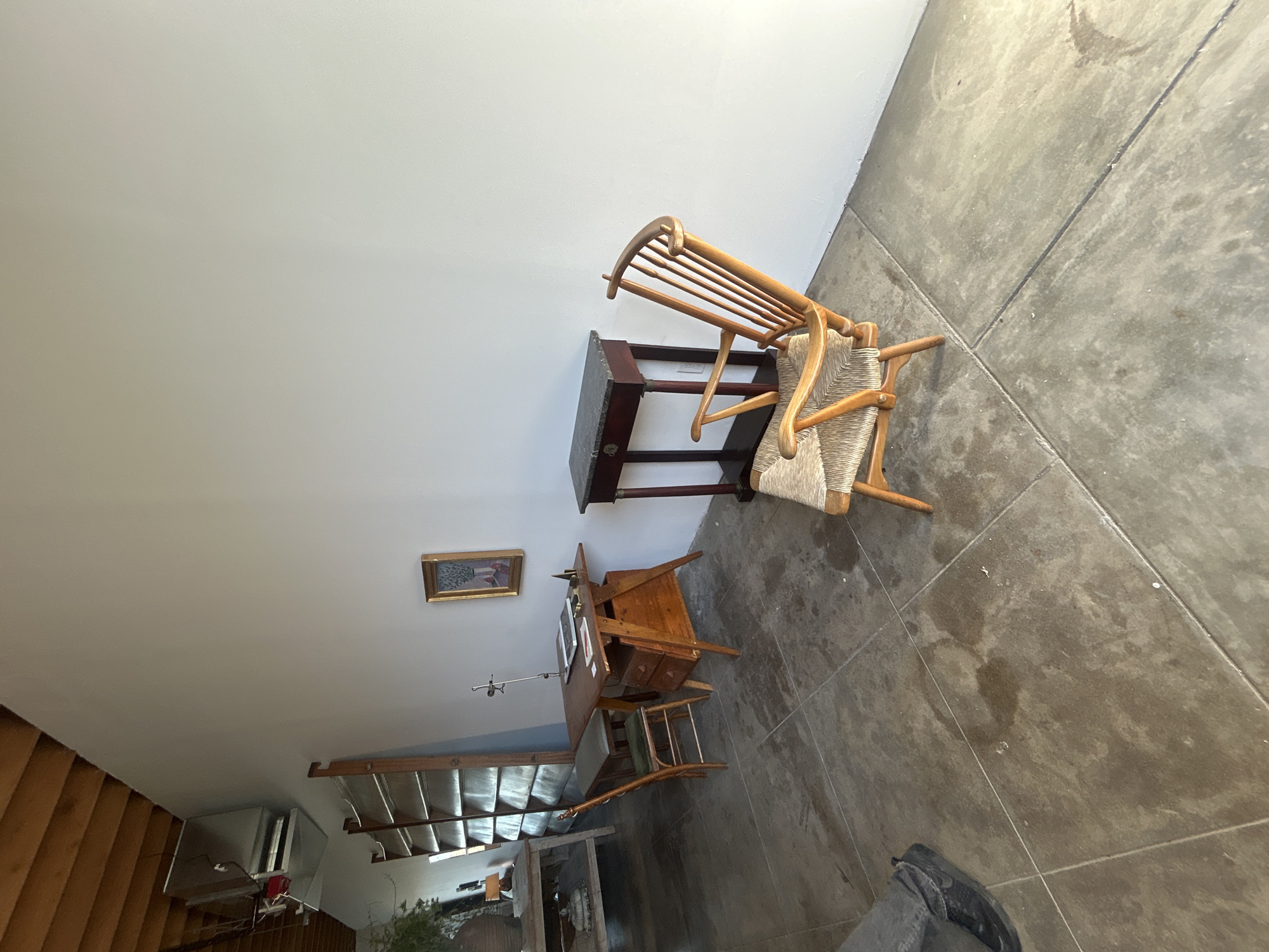 The image shows an interior with furniture, including a chair, a wooden desk, and a coat rack, along a wall with a framed picture. Further away, there's a staircase leading down. The location is unclear. The photograph lacks sufficient information to determine the location as Los Angeles, United States of America.