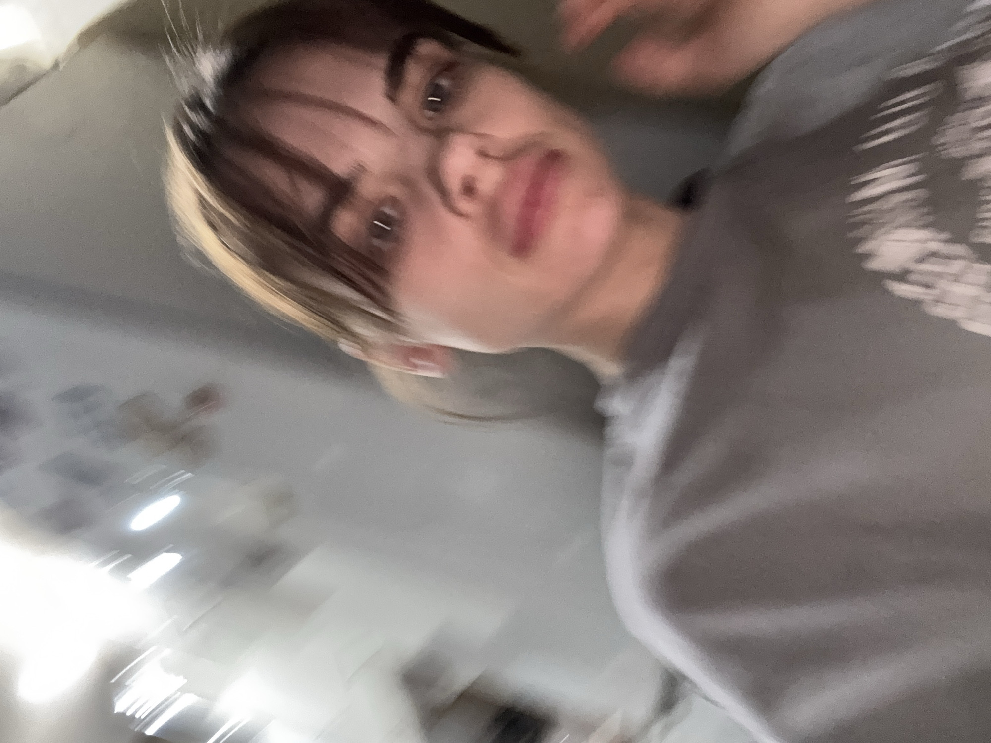 A close-up, blurred photograph shows a person with brown hair, highlighted blonde streaks, and bangs, looking towards the camera. The person is wearing glasses and a grey shirt. The background is blurry and indistinct. There are no discernable clues indicating that the location is in the city of Rostov-on-Don, Russia.