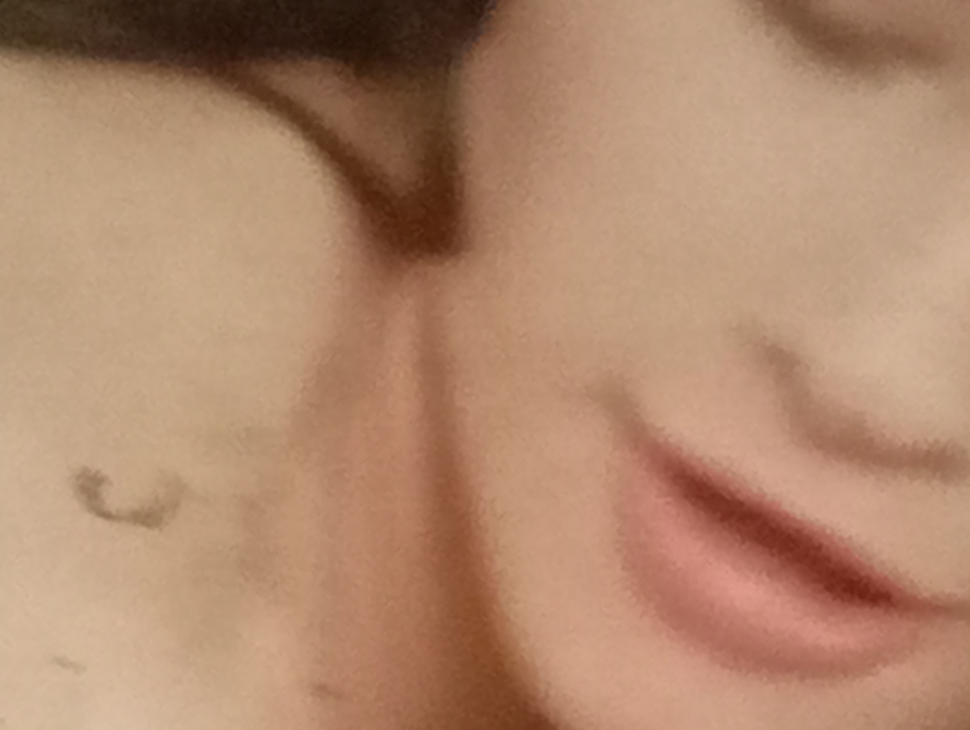 The image is a close-up, abstract shot of a person's face, focusing on the area around the mouth and cheek. The lighting is soft and diffused, creating a painterly effect. The skin tone is fair with subtle pink undertones, particularly on the lips, which appear to be slightly parted and possibly glossed. There is a faint shadow or mark on the left side of the cheek that forms a curved shape. The background is a blur of warm, neutral tones, suggesting an indoor environment or soft focus outdoor setting. No specific location in Sofiivska Borshchahivka, Ukraine, can be identified from this image.