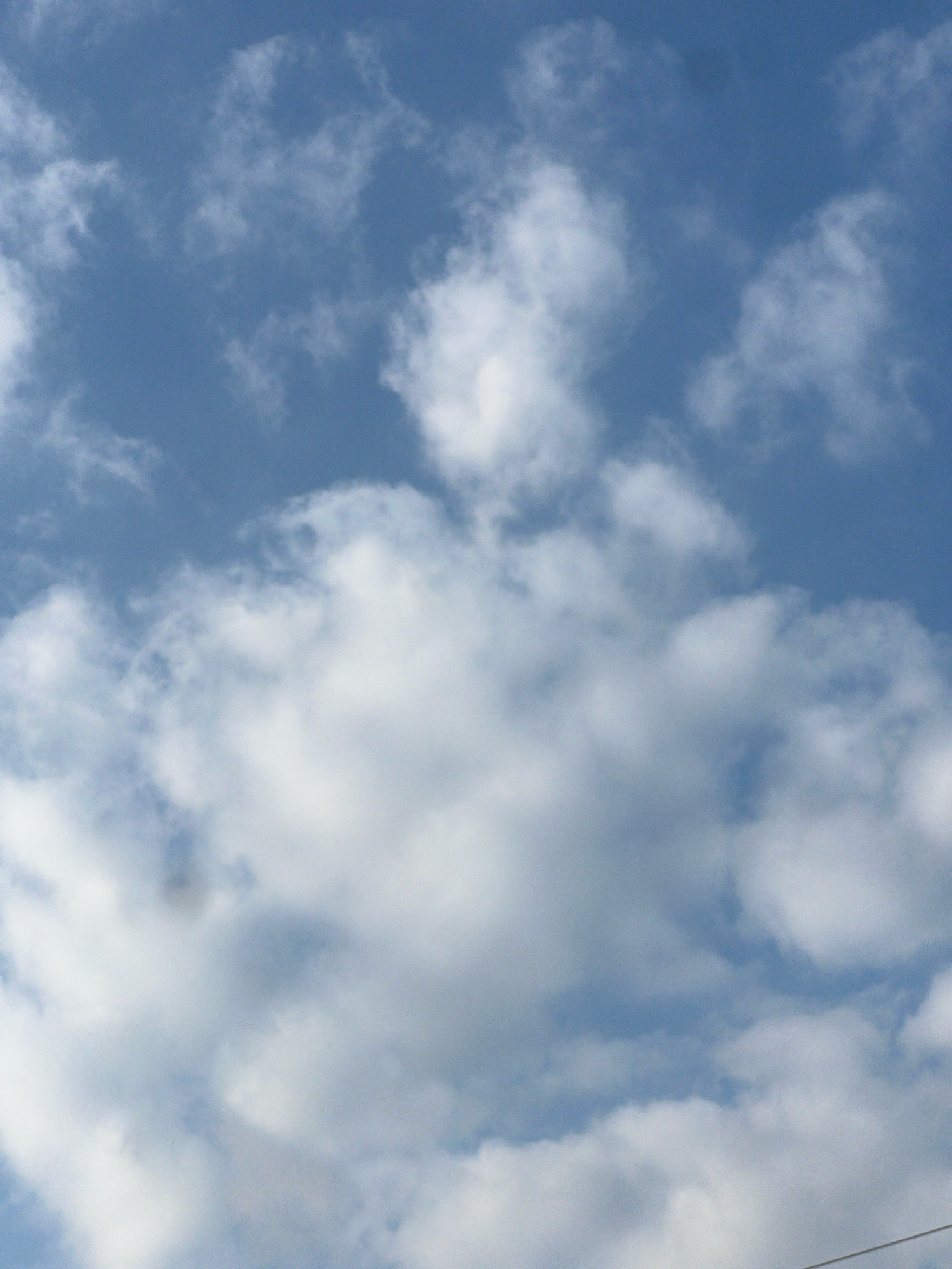 The image depicts a clear blue sky filled with white, fluffy clouds. There are no visible buildings, people, or objects within the frame. The focus is solely on the atmospheric conditions. The scene appears to be an outdoor environment, likely taken during the daytime. The cloud formations suggest fair weather. No specific landmarks or details indicating the city of Kuta, Indonesia are present.