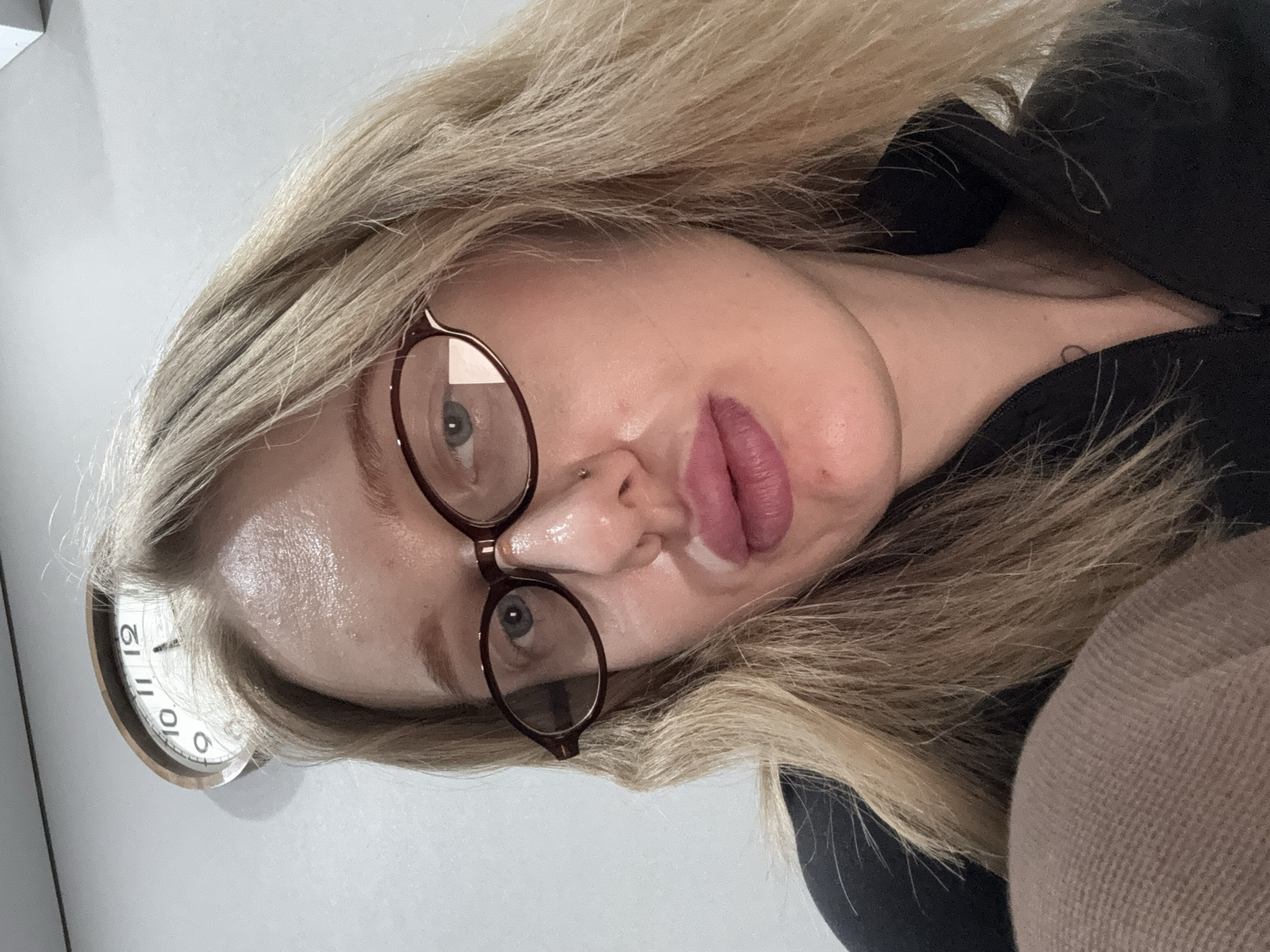 A selfie-style photograph features a blonde woman wearing eyeglasses. A portion of a clock is visible in the background. There is no information to determine a location in Kuleshovka, Russia.