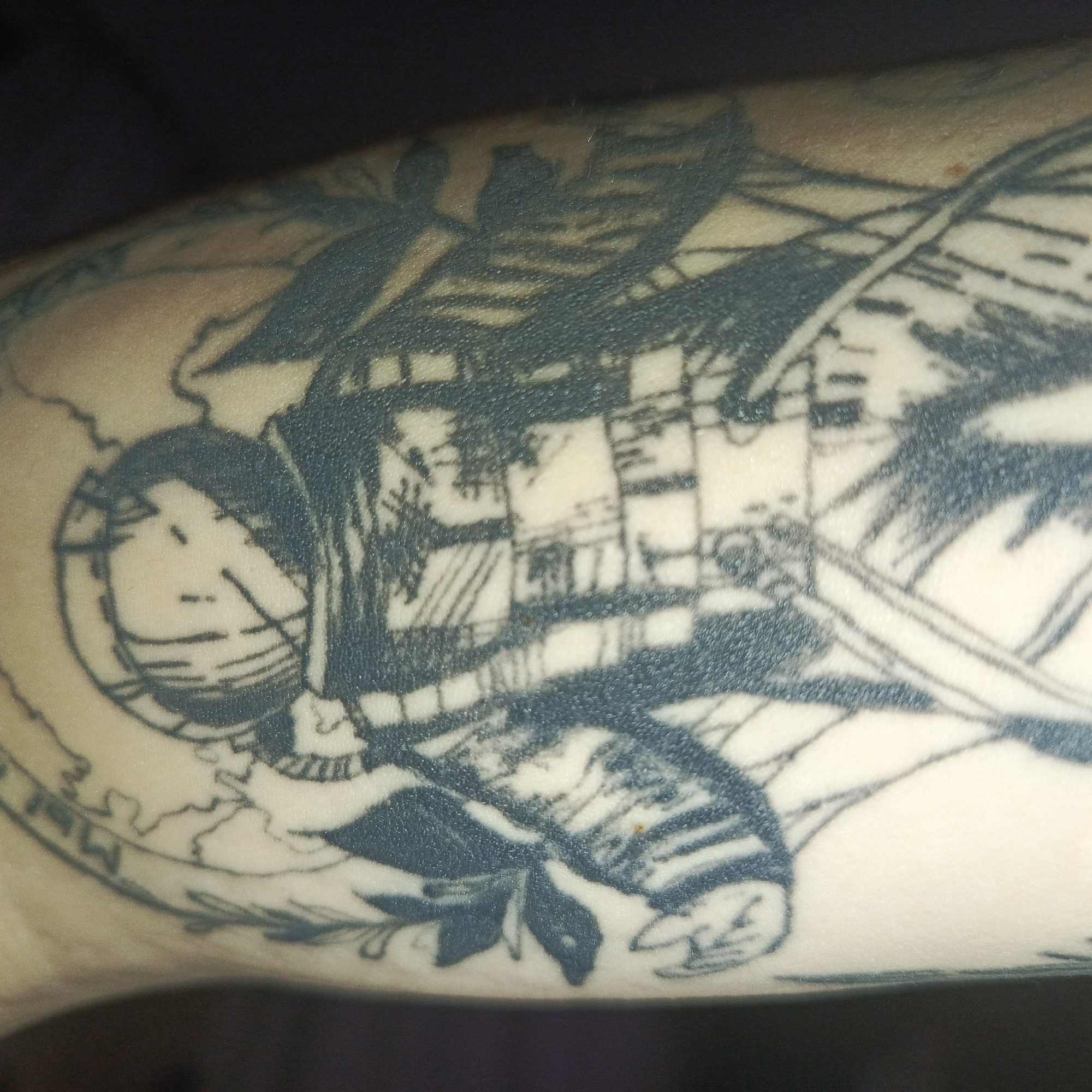 The image shows a tattoo on a person's arm. The tattoo depicts a stylized image of the city of Chaikovsky, Russia. It appears to include an outline of the city's layout or landmarks within a circular border that includes some text, and possibly some botanical elements. The style of the tattoo is line-work, predominantly in dark ink.