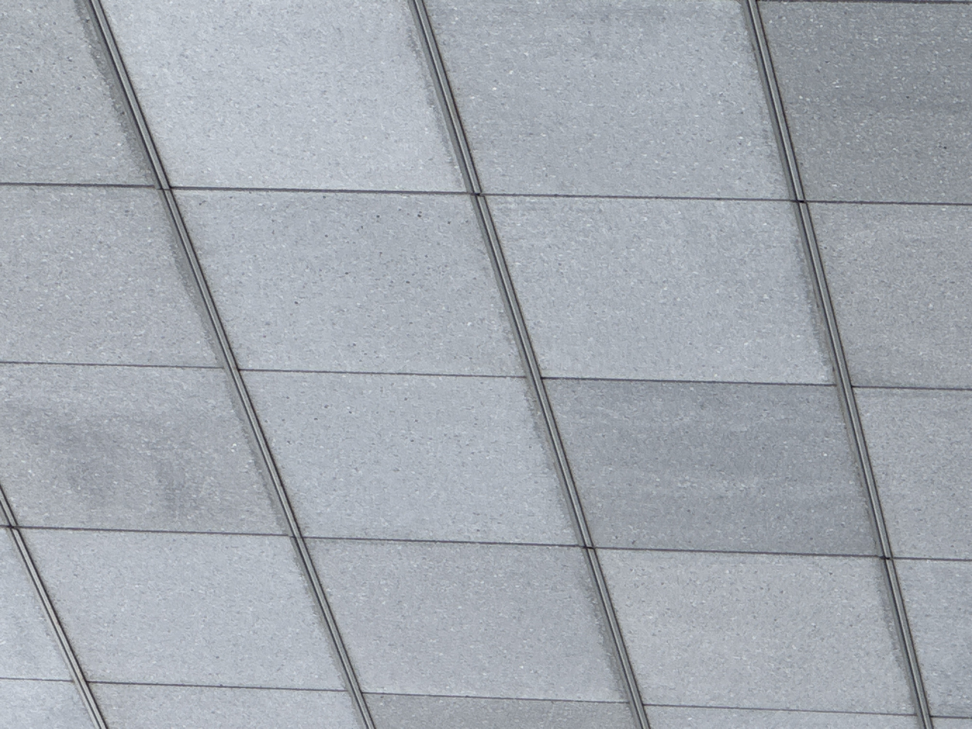 The image depicts a section of a gray tile wall, possibly part of the Moscow International Business Center (Moscow City) in Russia. The tiles are square and arranged in a grid pattern, with dark gray or black grout lines. The tiles appear to be made of a textured, speckled material. The perspective is from below, looking up at the wall at an angle. There are no people or other discernible objects in the scene.