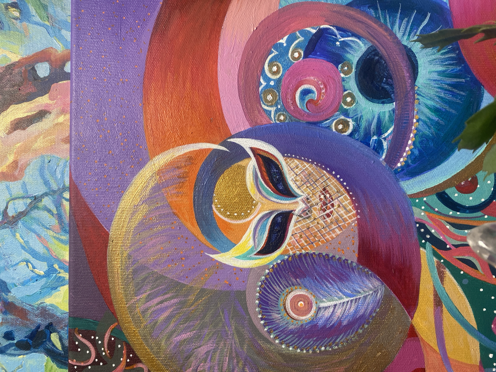 The image is a close-up shot of an abstract painting on canvas. The style is vibrant and colorful, featuring a variety of shapes, including spirals, circles, and feather-like forms. Colors present are purple, orange, pink, blue, and gold. The painting has a layered, textured appearance. There are no people visible in the frame, and no specific location can be inferred from the image. The painting contains details, such as white dots, lattice patterns, and small decorative swirls.