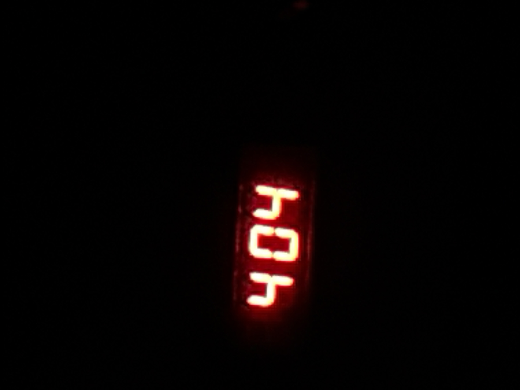 The image displays a close-up view of a digital display showing the numbers "404" in bright red against a dark background. The display appears to be part of an electronic device, possibly a clock or a status indicator. The resolution of the image is low, and the lighting is dim, making it difficult to discern the exact nature of the device or its surroundings. There are no people, animals, or other recognizable objects present in the scene. The image is devoid of any contextual information that would suggest its location within the city of Бұлақты, Kazakhstan, or any specific urban setting.