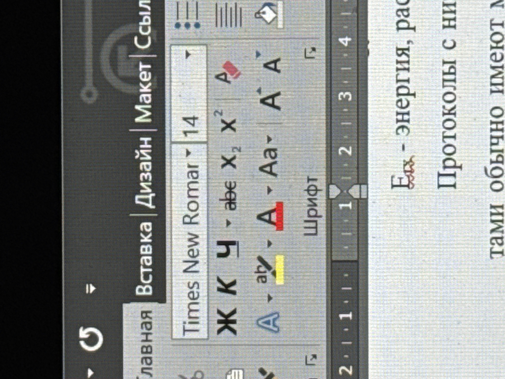 The image shows a portion of a computer screen displaying the user interface of a word processing program, likely Microsoft Word, with a document open. The interface is in Russian. The ribbon at the top displays tabs labeled "Главная" (Home), "Вставка" (Insert), "Дизайн" (Design), "Макет" (Layout), and "Сссыл" (References). The "Home" tab is active, revealing font options such as "Times New Roman" and size "14." Icons for bold, italic, underline, and text effects are visible, as well as font color and highlighting options. A formatting ruler is also displayed at the top of the document. The document text includes the phrase "Елх - энергия, рас" and "Протоколы с ни."
The text "тами обычно имеют м" is also visible.
There is no mention in the image of Izhevsk, Russia.