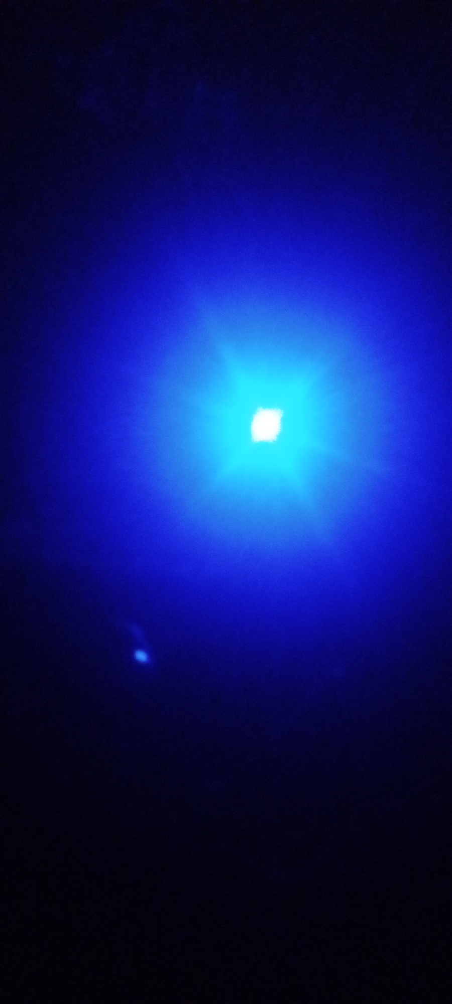 A single bright blue light dominates the center of the image, appearing to be the primary source of illumination in a very dark environment. A smaller, less intense blue light is visible in the lower left quadrant. The overall setting appears to be nighttime, although the specific location in Sabon Tasha, Nigeria, or any other details about the environment, people, objects, or actions, cannot be determined from this image alone.