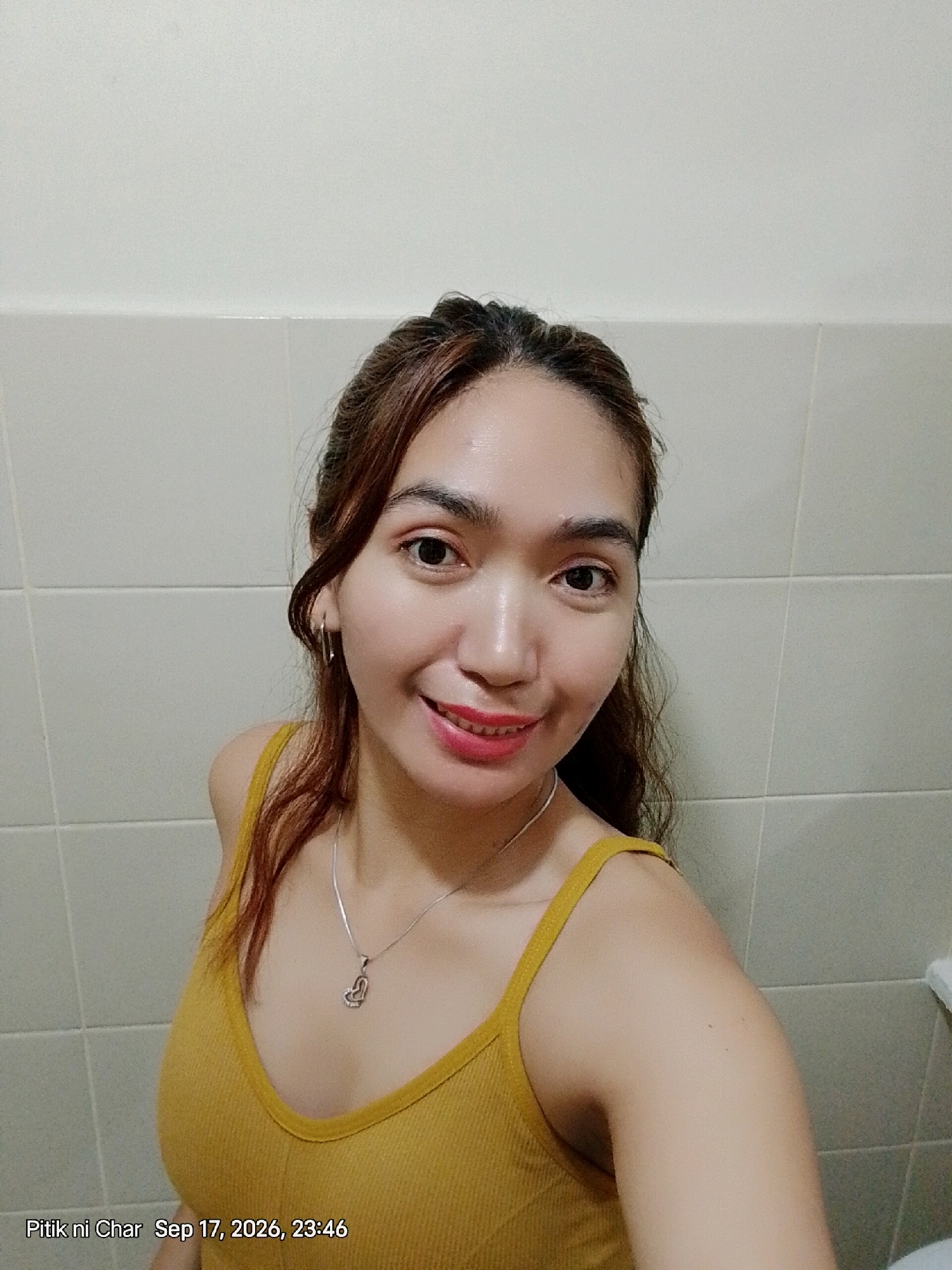 A young woman with brown hair and brown eyes is smiling at the camera. She is wearing a yellow tank top and a silver necklace with a heart-shaped pendant. The background is a tiled wall. A timestamp in the lower left corner reads "Pitik ni Char Sep 17, 2026, 23:46". There are no discernable landmarks or contextual elements to determine the specific location within Davao City, Philippines, or any other city.