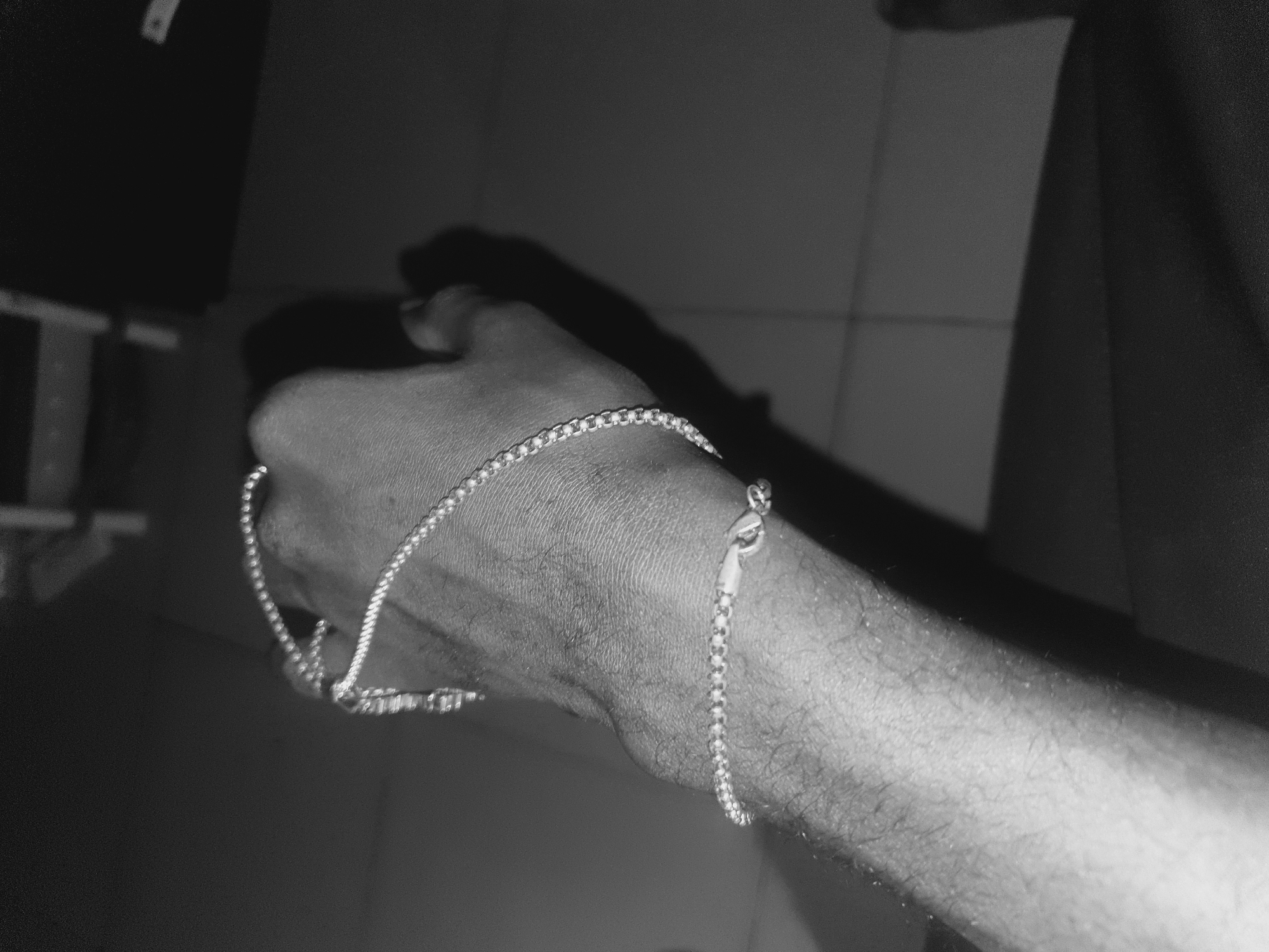 A black and white close-up shot shows a person's arm and hand holding a silver chain. The chain is draped across the hand and wrist. The background is dark and blurry, making it difficult to discern any environmental details. There is no specific information available to identify the location as Lokoja, Nigeria. The description is limited to the visible content of the image.