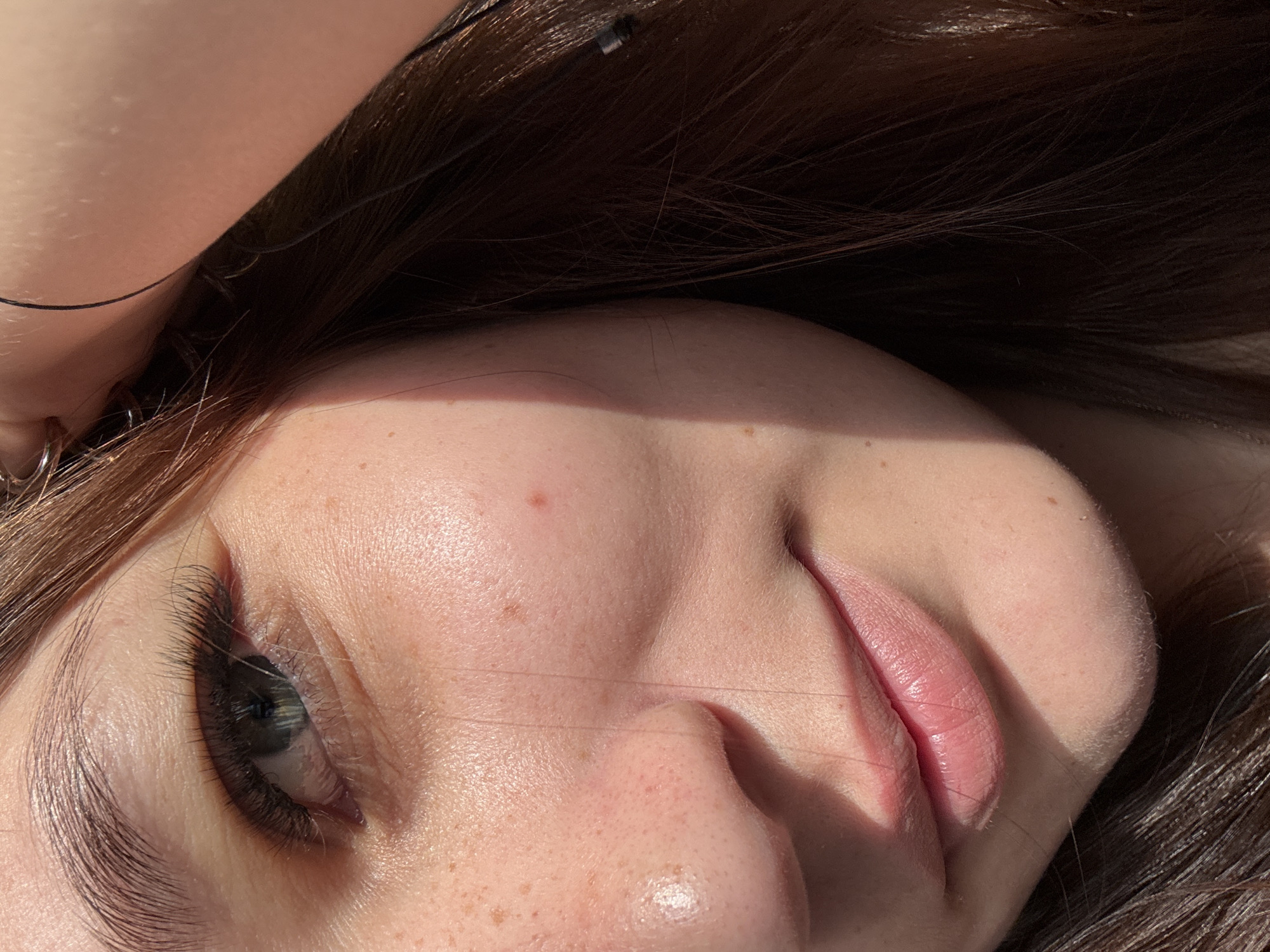 The image is a close-up shot of a young person's face, focusing on their eye, nose, and lips. Sunlight is casting a shadow across their cheek. The person has brown hair and appears to have freckles on their skin. There are no discernible details about the location in Novokuznetsk, Russia, as the image is solely focused on the individual's face and does not contain any environmental cues.