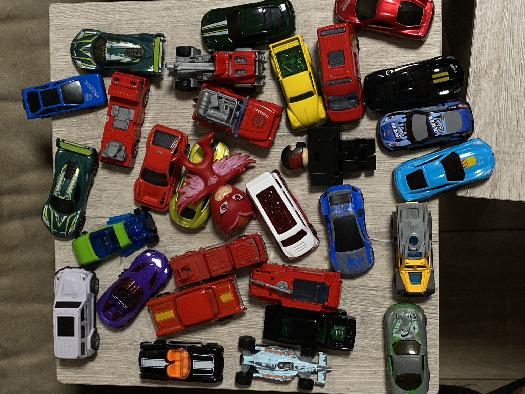 The image shows a collection of toy cars on a light-colored wooden surface. There are approximately 30 toy cars of various colors, shapes, and sizes. The cars include sports cars, trucks, and other vehicle types. There are no people visible in the image. The environment appears to be indoors. There is no information about the location in the city of Vysokoye, Russia.