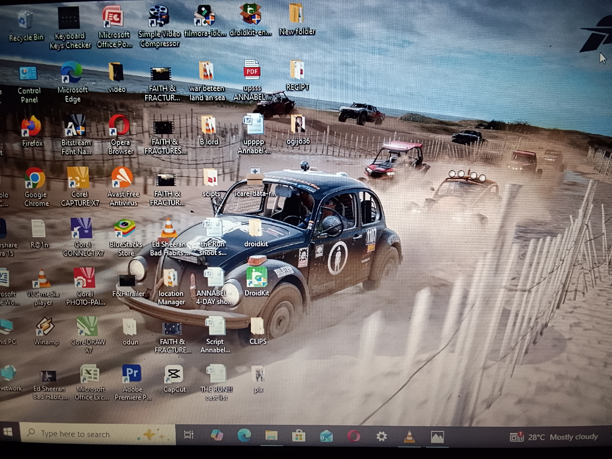 The image is a screenshot of a Windows desktop. The background wallpaper features a dusty off-road race with multiple buggies or similar vehicles driving through a sandy landscape. The desktop is cluttered with various application icons and file shortcuts, including "Recycle Bin", "Microsoft Edge", "Firefox", "Google Chrome", "Corel Capture X7", "Avast Free Antivirus", "VLC media player", "Adobe Premiere Pro", and numerous files named "FAITH & FRACTUR...", "ANNABEL...", "Ed Sheeran Bad Habits...", "THE RUN!!!", among others. The taskbar shows the Windows start button, search bar, system tray with icons for network, sound, battery, and date/time with the temperature displayed as 28°C and the weather as "Mostly cloudy".
There is no information suggesting this screenshot relates to Adankolo, Nigeria.