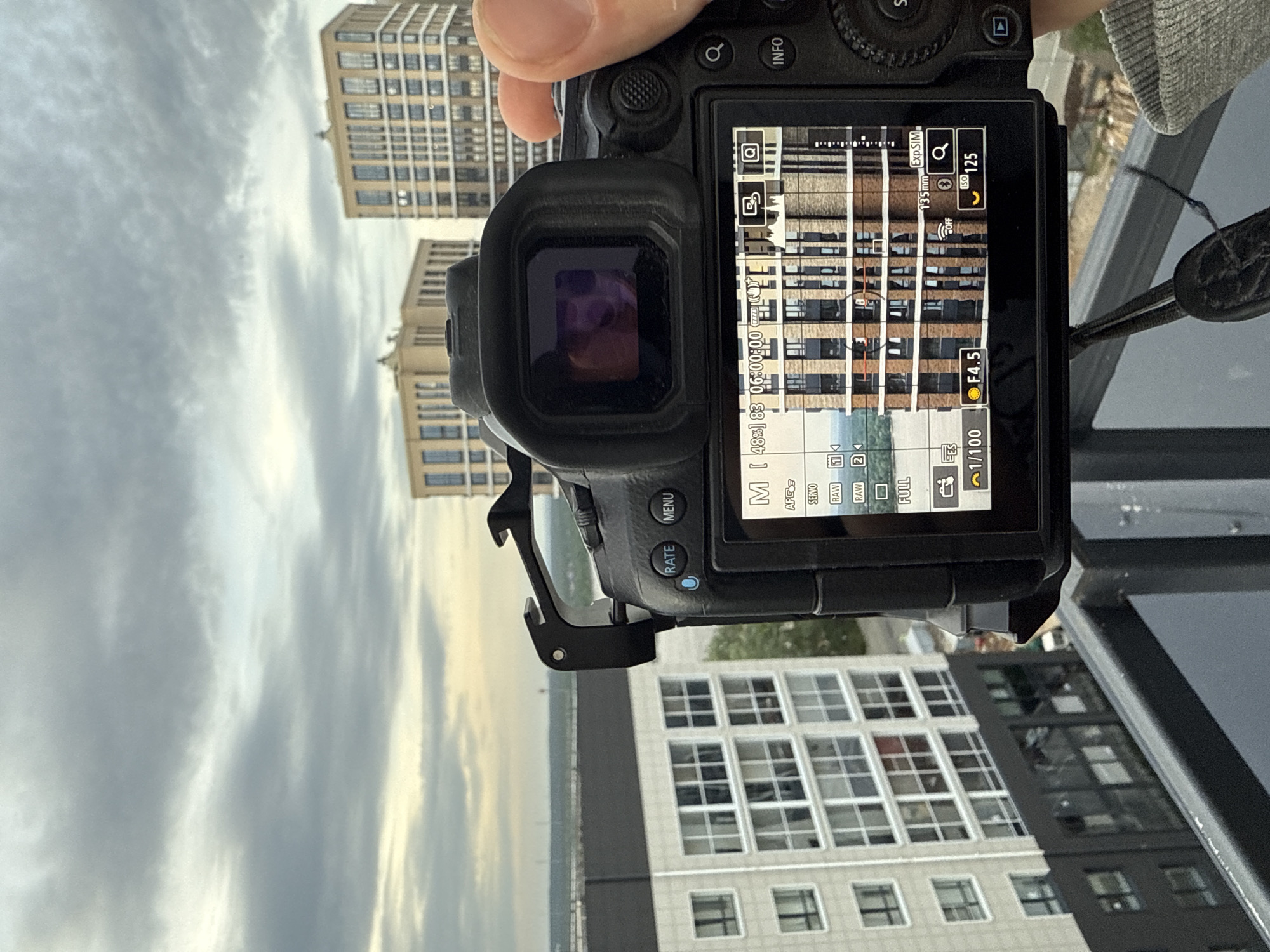 A camera is pointed up towards two tall buildings, capturing the sky, and the screen of the camera shows the images recently taken. The camera settings are as follows: 1/100, F4.5, ISO 125. The location is not possible to determine based on the image provided.