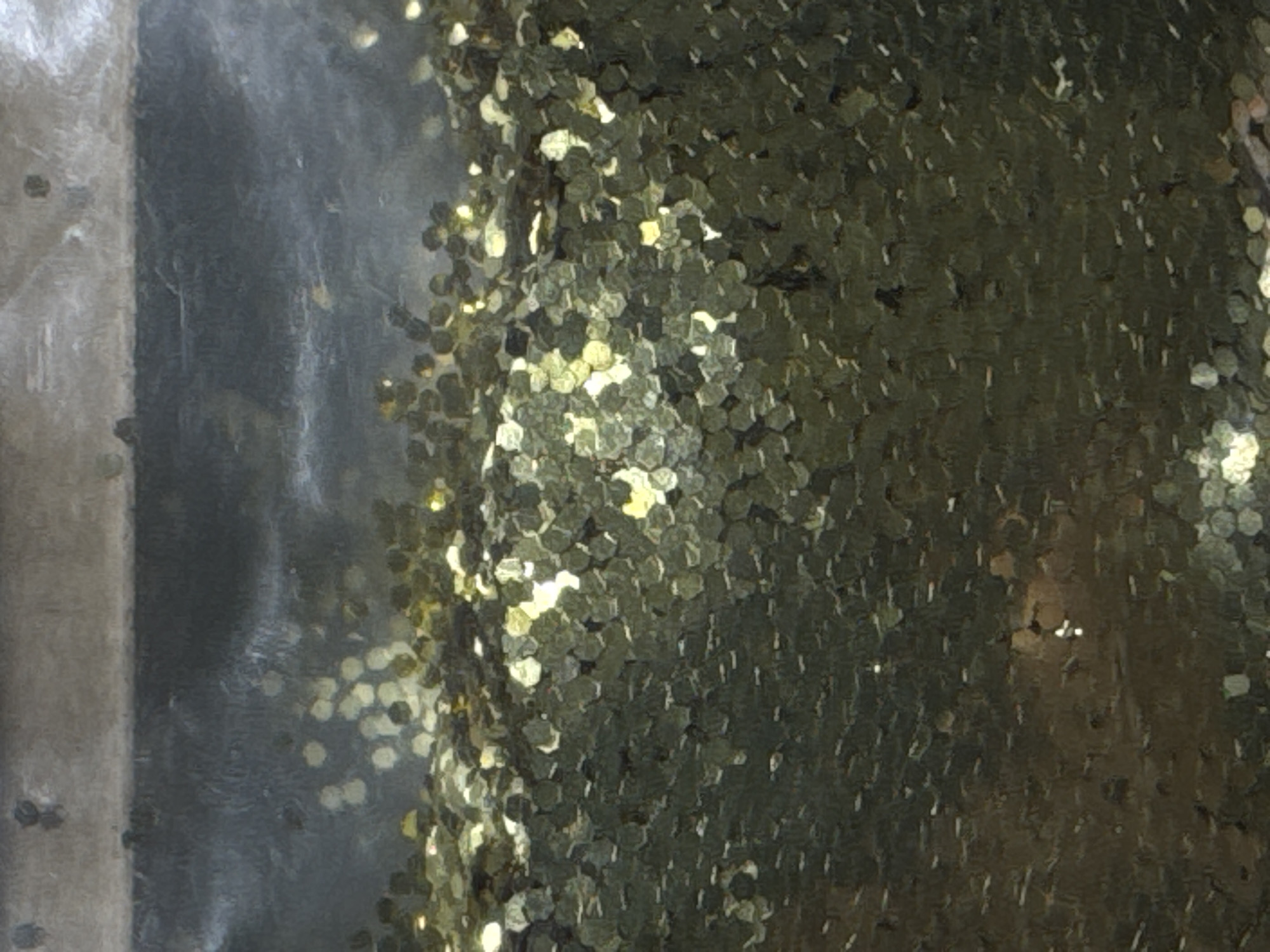 The image shows a close-up of gold glitter within a clear container. The glitter is hexagonal and appears to be suspended in a liquid, though the liquid itself is not clearly visible. The lighting creates bright reflections on the glitter. There are no discernible features indicating a specific location in Moscow, Russia.