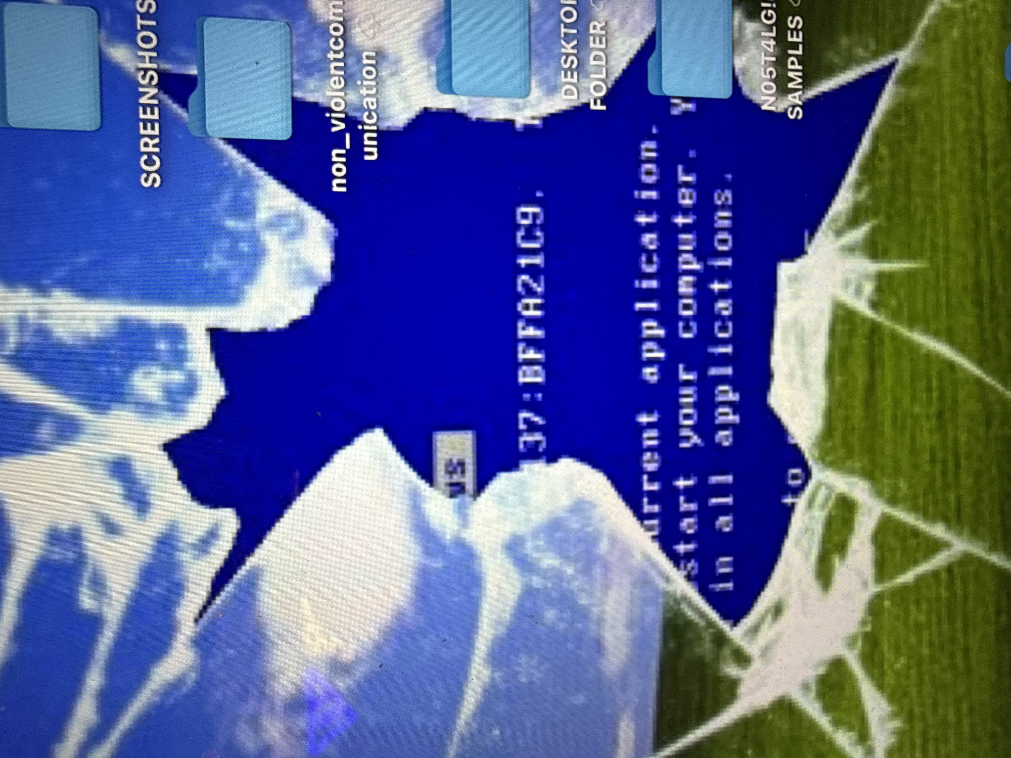 The image depicts a computer screen with the Windows Blue Screen of Death (BSOD) displayed. The screen shows the error message containing information such as "BFFA21C9" and mentions "current application" and "start your computer." Overlaid on the BSOD are icons of computer folders labelled "SCREENSHOTS," "non_violentcommunication," "DESKTOP FOLDER," and "N05T4LG! SAMPLES." The image is further disrupted by a visual pattern that appears to be cracks.
There is no location in the city of London, United Kingdom to be found from this image.