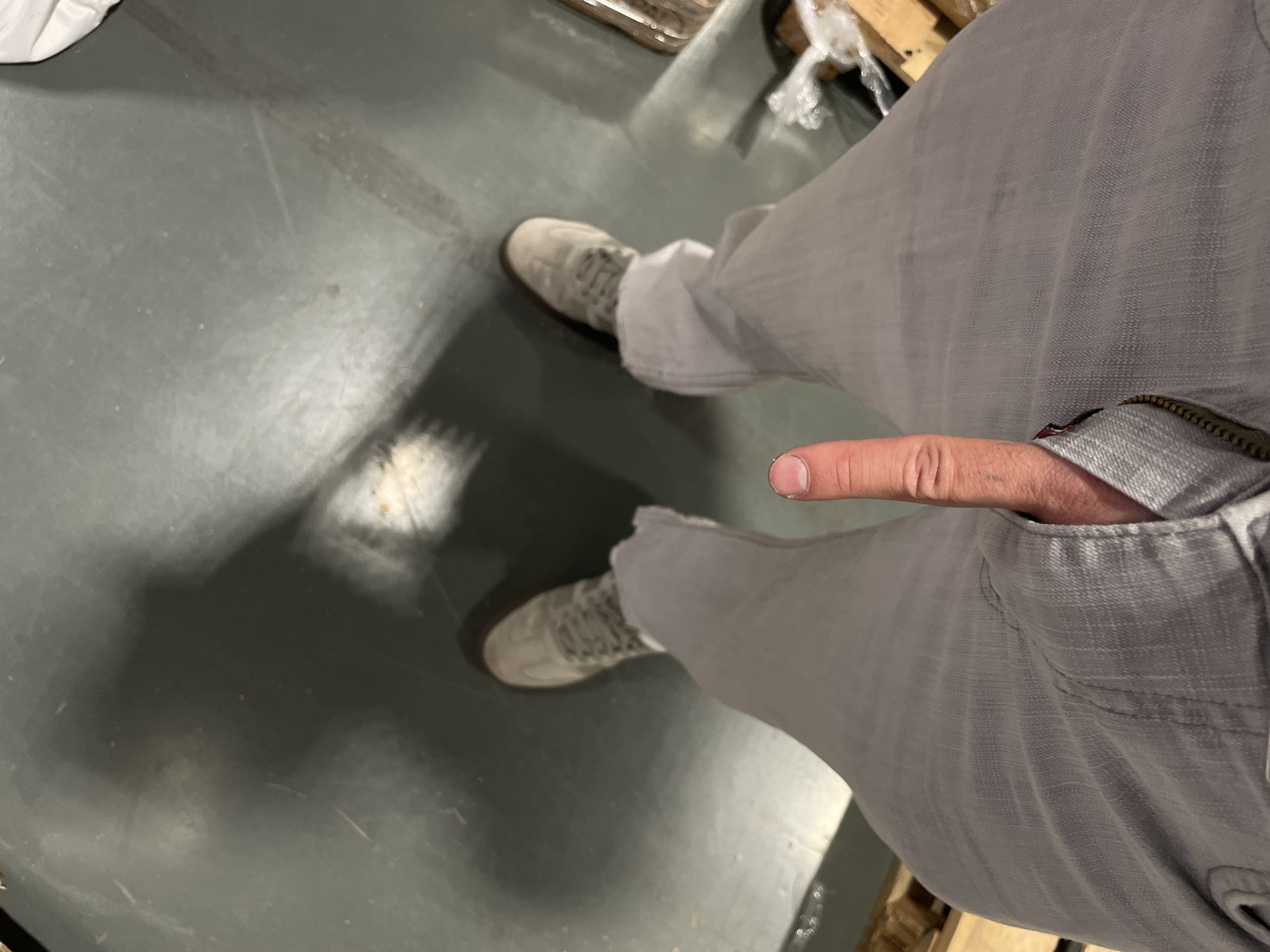 A top-down shot depicts a person wearing gray pants and gray shoes standing on a gray floor. The person's right hand is near the open zipper of the pants. The location is Unknown, Unknown.