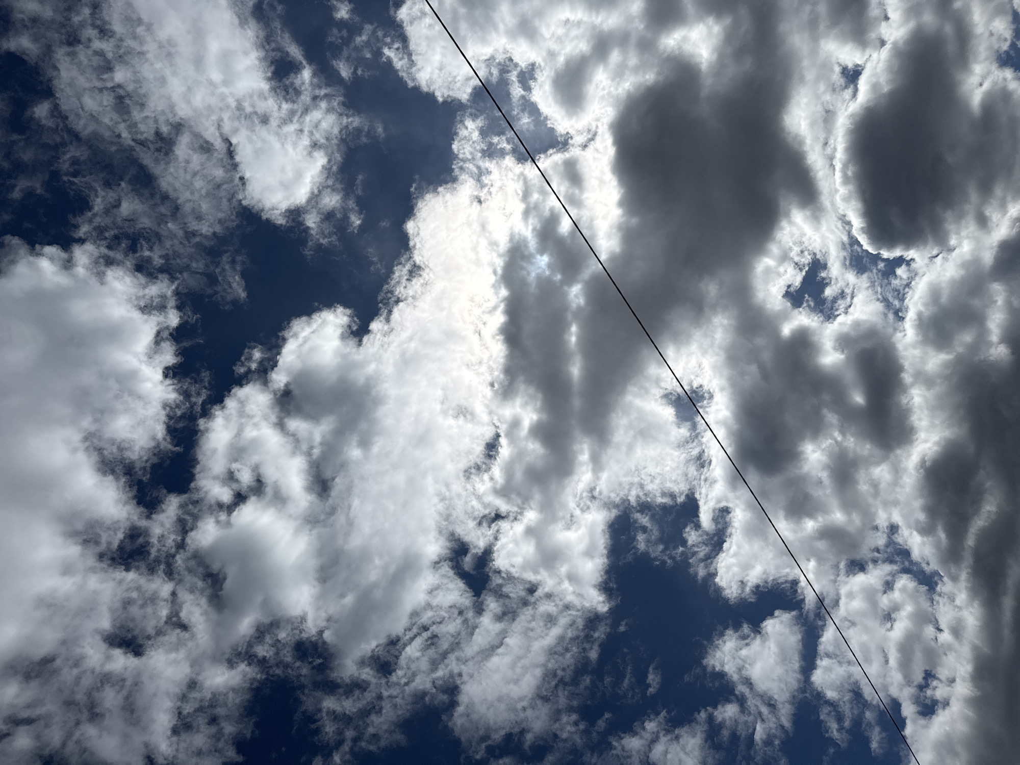 The image shows a view of the sky with scattered clouds and a dark blue background. A single black wire runs diagonally from the upper right to the lower left of the frame. No people or objects are visible besides clouds and a wire. The location of the city Chaikovsky, Russia is not supported by what is shown in the image.