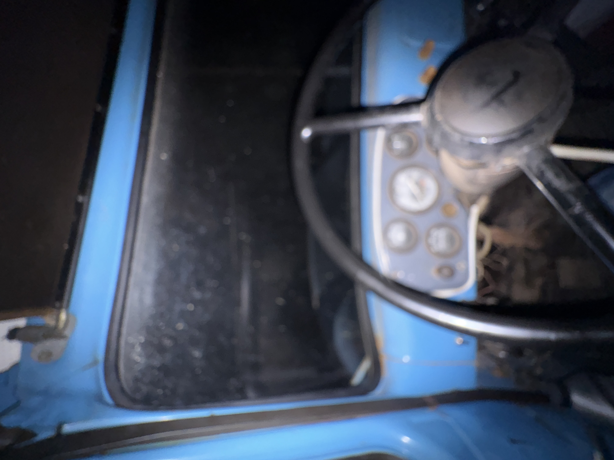 The image shows the interior of an old, blue vehicle, likely a truck or a tractor, with a focus on the dashboard and steering wheel. The dashboard features several circular gauges, some of which are blurry but appear to have needles indicating readings. The steering wheel is black and appears worn. The interior of the vehicle seems somewhat dilapidated, with visible rust on the blue paintwork near the window frame. The overall lighting is dim, suggesting it might be nighttime or the interior is poorly lit. The environment outside the vehicle is dark and indistinct. There are no people visible in the image. The location of Kechut, Armenia, is not discernible from the visual information presented in the image.