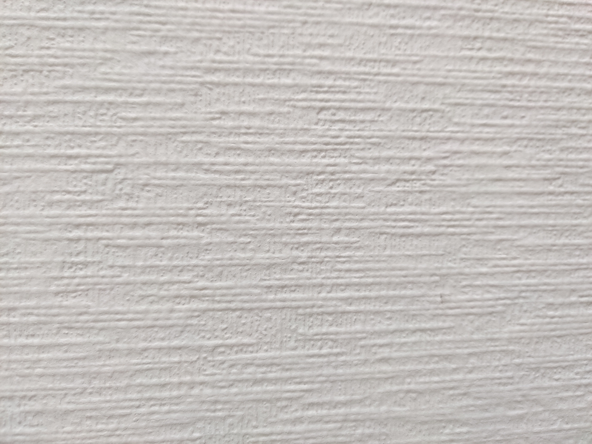 A close-up, full-frame shot displays a textured, off-white surface that appears to be wallpaper or painted drywall. The texture is characterized by subtle, vertical, ridged striations. The lighting creates soft shadows that accentuate the raised areas, giving the surface a slightly uneven, tactile quality. There are no people, objects, or discernible environmental features visible in the image. The image is a neutral and abstract representation of a wall surface, lacking any specific context of location, including Yekaterinburg, Russia.