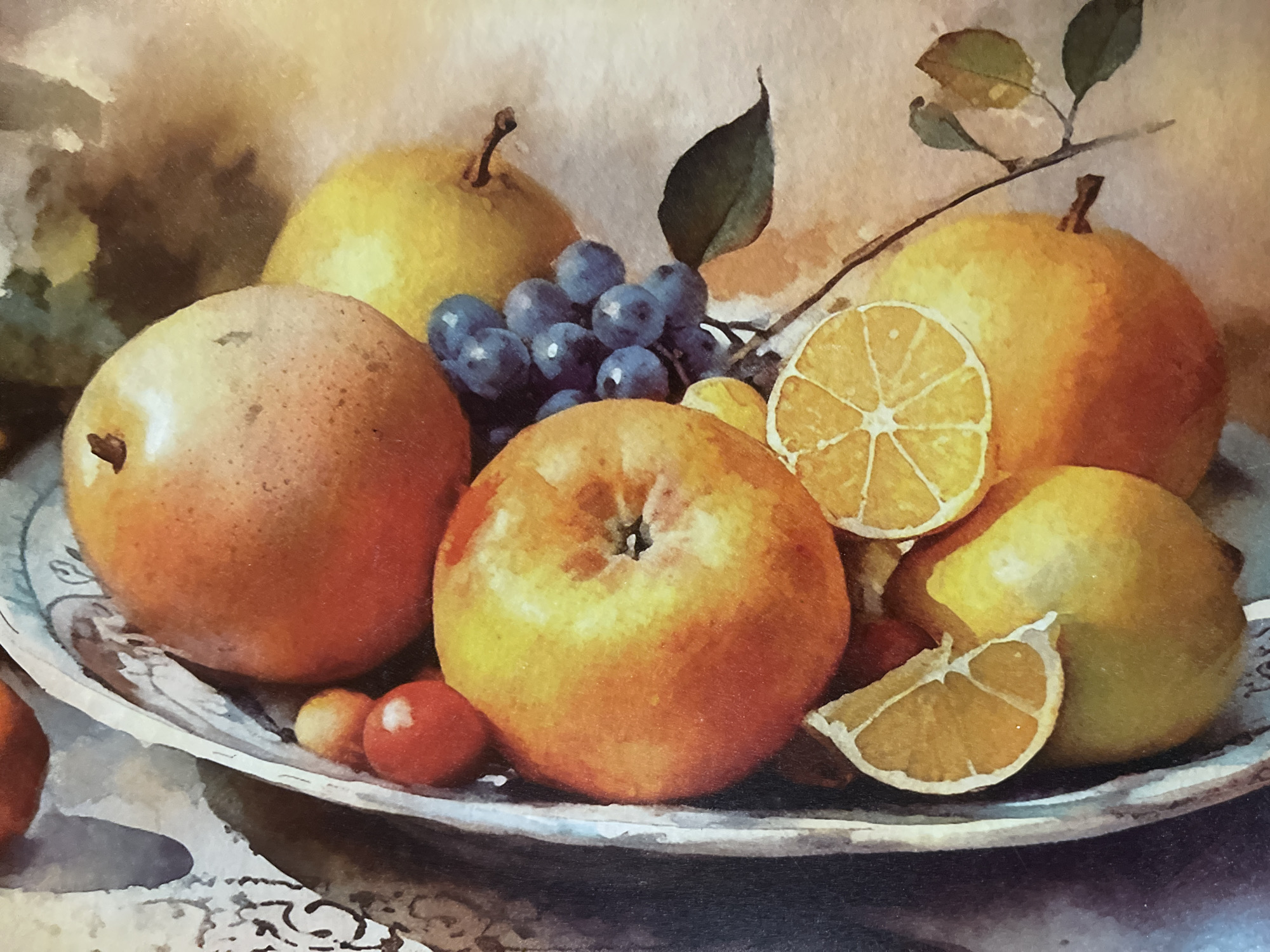 The image is a close-up, top-down watercolor painting of a still life featuring a variety of fruits arranged in a decorative metal bowl. The fruits include an apple, two pears, a cluster of dark blue grapes, two slices of lemon, a few small red berries, and other round fruits that appear to be oranges or peaches. The bowl has an ornate, textured edge. The background is a softly blended wash of warm, earthy tones. There are no people or visible actions depicted in the image. The painting style is impressionistic, with visible brushstrokes and a soft focus. The scene is static and decorative. There is no information in the image that suggests it is located in Minsk, Belarus.