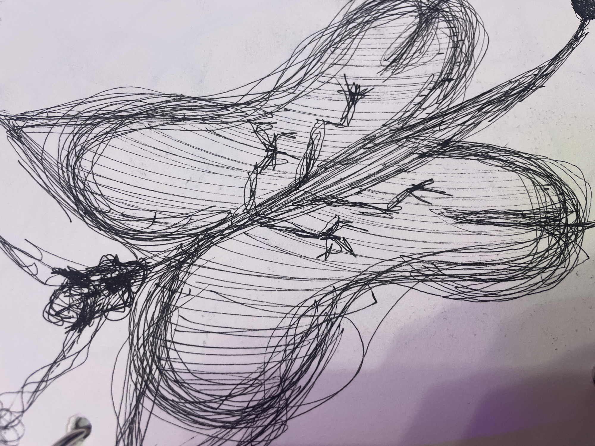 The image is a close-up, black and white sketch on white paper. The sketch depicts a stylized, abstract figure that appears to be a person with outstretched arms and possibly wings or flowing fabric. The lines are gestural and energetic, with a strong emphasis on scribbled textures. There is a metallic ring visible on the left edge of the paper, suggesting it is part of a sketchbook or binder. The lighting in the image creates a soft, purple hue in the background on the left side, which is likely a reflection from an external light source. There are no discernible elements that place this image in the city of Sinyavino, Russia.