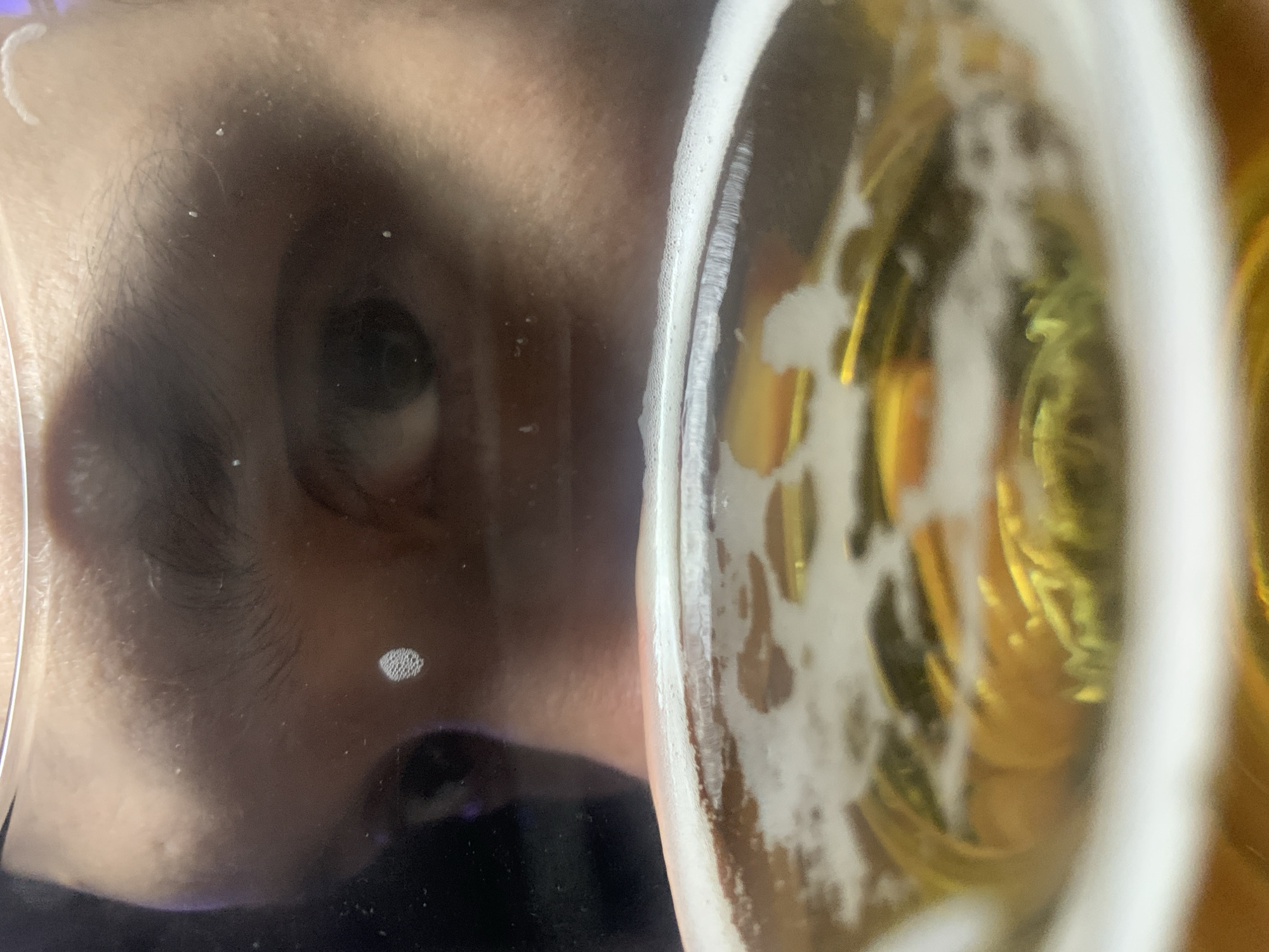 A close-up, distorted view features a person's eye and part of their face reflected in the glass of a beer. The beer is light-colored with a frothy head. The person's face is pressed against the glass, causing the distortion. The location cannot be determined from the image, therefore the location of Chaikovsky, Russia cannot be verified.