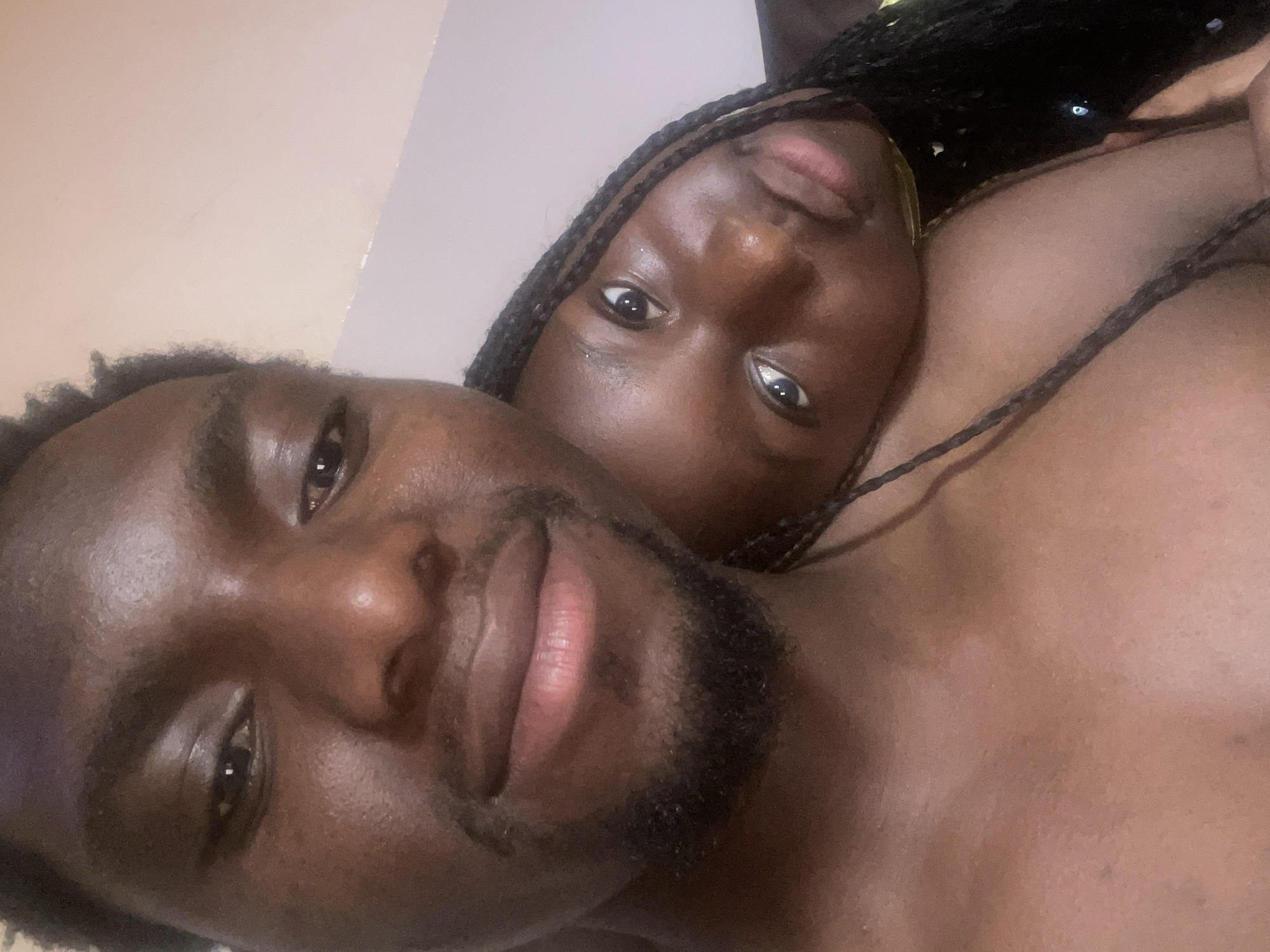 A close-up photograph shows two dark-skinned individuals posing closely together. The person on the left is a man with short, dark hair and a beard. The person on the right is a woman with braided hair. The photo appears to be taken in an indoor setting. There is no information to suggest the image was taken in the city of Jos, Nigeria.