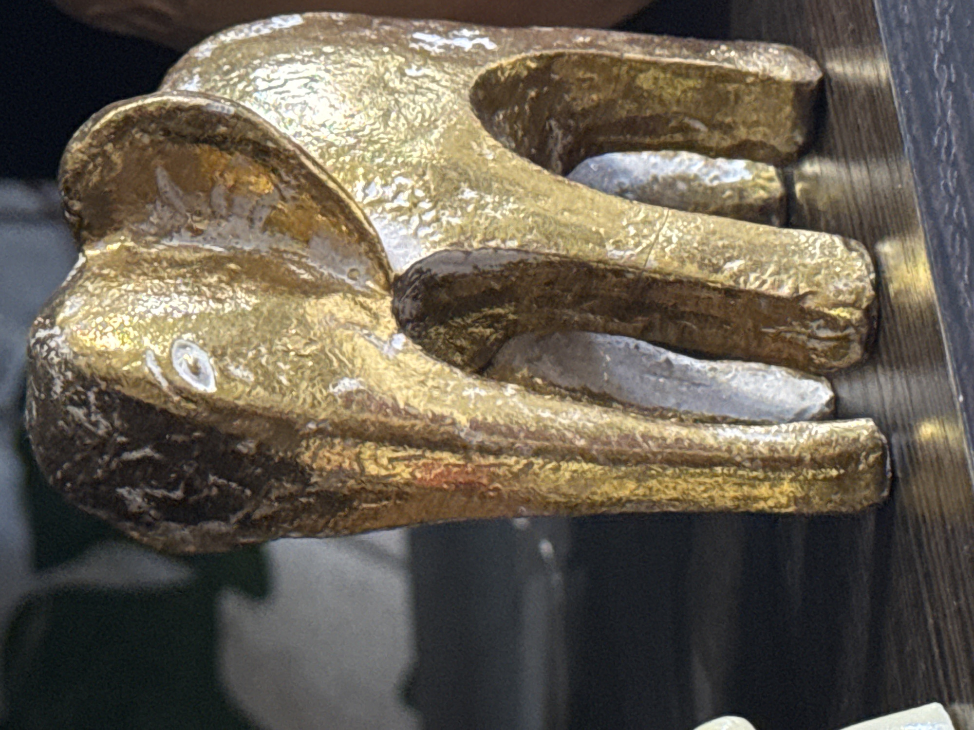 A gold-colored decorative figure of an elephant is shown in a close-up shot. The figure appears to be resting on a dark surface near a wooden edge. The elephant has a textured surface, with some white paint or material showing through the gold finish. The background is slightly blurred and obscured. There is no indication of the city of Kladovitsy, Russia.