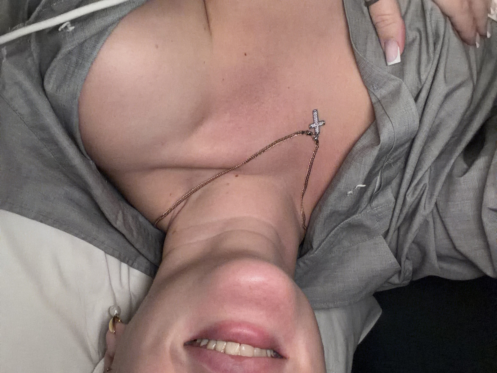 A woman is lying down, wearing a gray button-down shirt and a cross necklace. Her face is visible, showing her mouth slightly open. The background appears to be bedding, possibly a pillow. There's no indication of the location being Moscow, Russia.