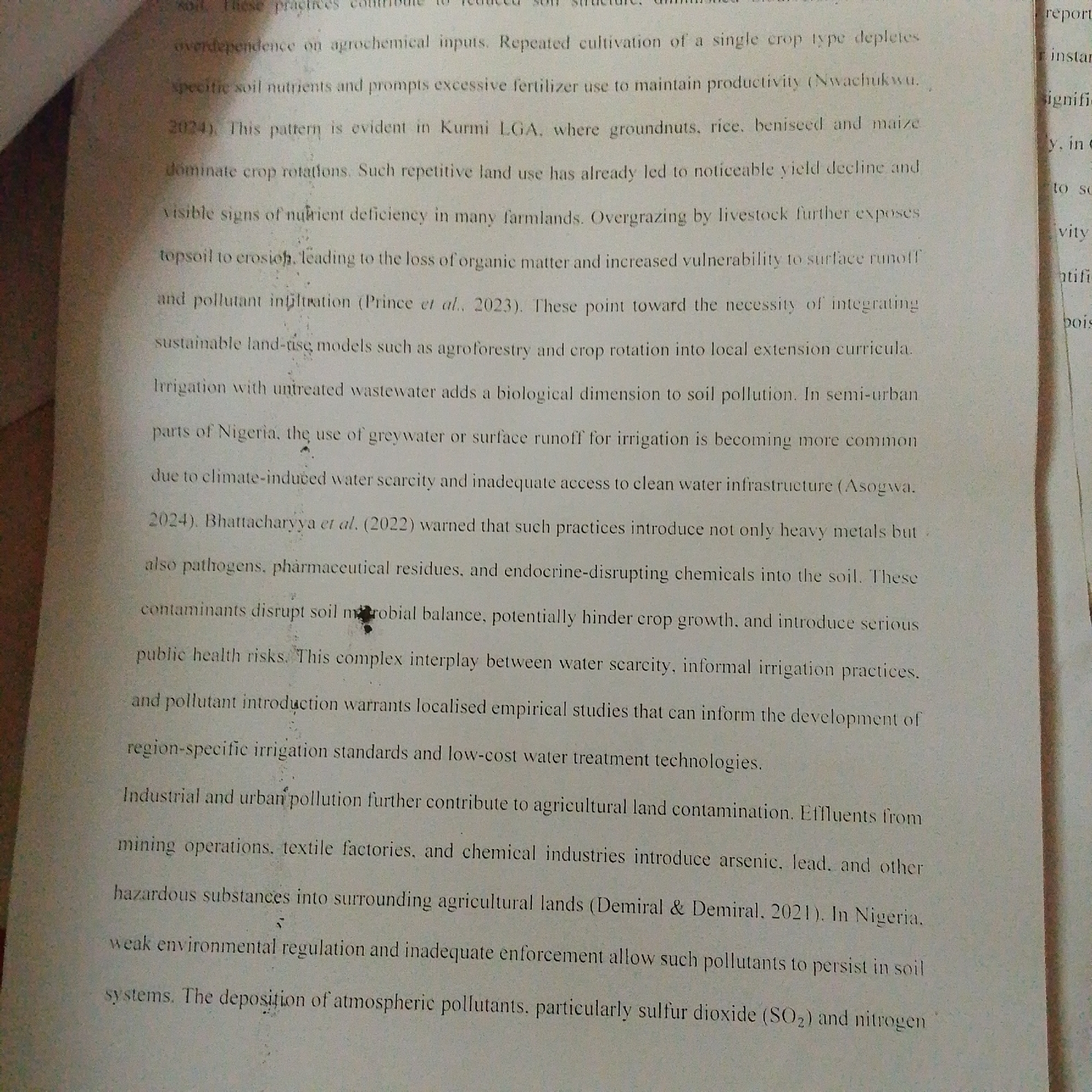 The image contains a close-up, top-down view of a document with text printed on it. The text discusses agricultural practices, soil pollution, and irrigation in Nigeria, specifically mentioning Kurmi LGA and Jalingo. It details issues like overdependence on agrochemicals, repetitive crop cultivation leading to nutrient deficiency and yield decline, and the impact of livestock overgrazing. The document also addresses the contamination of soil and water from industrial and urban sources, including heavy metals, pharmaceutical residues, and atmospheric pollutants. There are no people, subjects, or objects other than the document itself visible in the image.