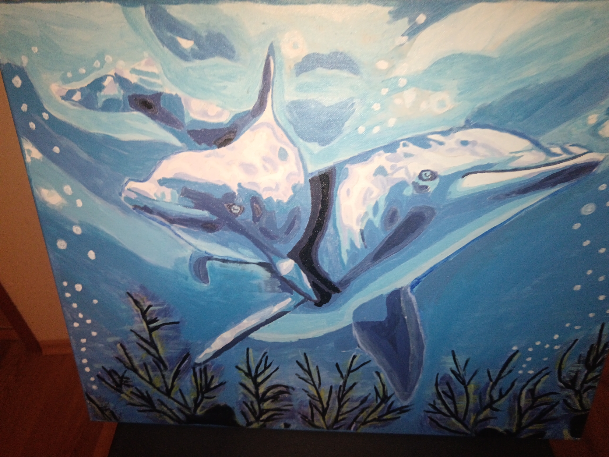The image shows a painting of two dolphins swimming underwater. The dolphins are rendered in shades of blue and white. Below the dolphins, there are seaweed-like plants in dark colors. White dots are scattered throughout the blue background, representing bubbles. The location is unspecified.