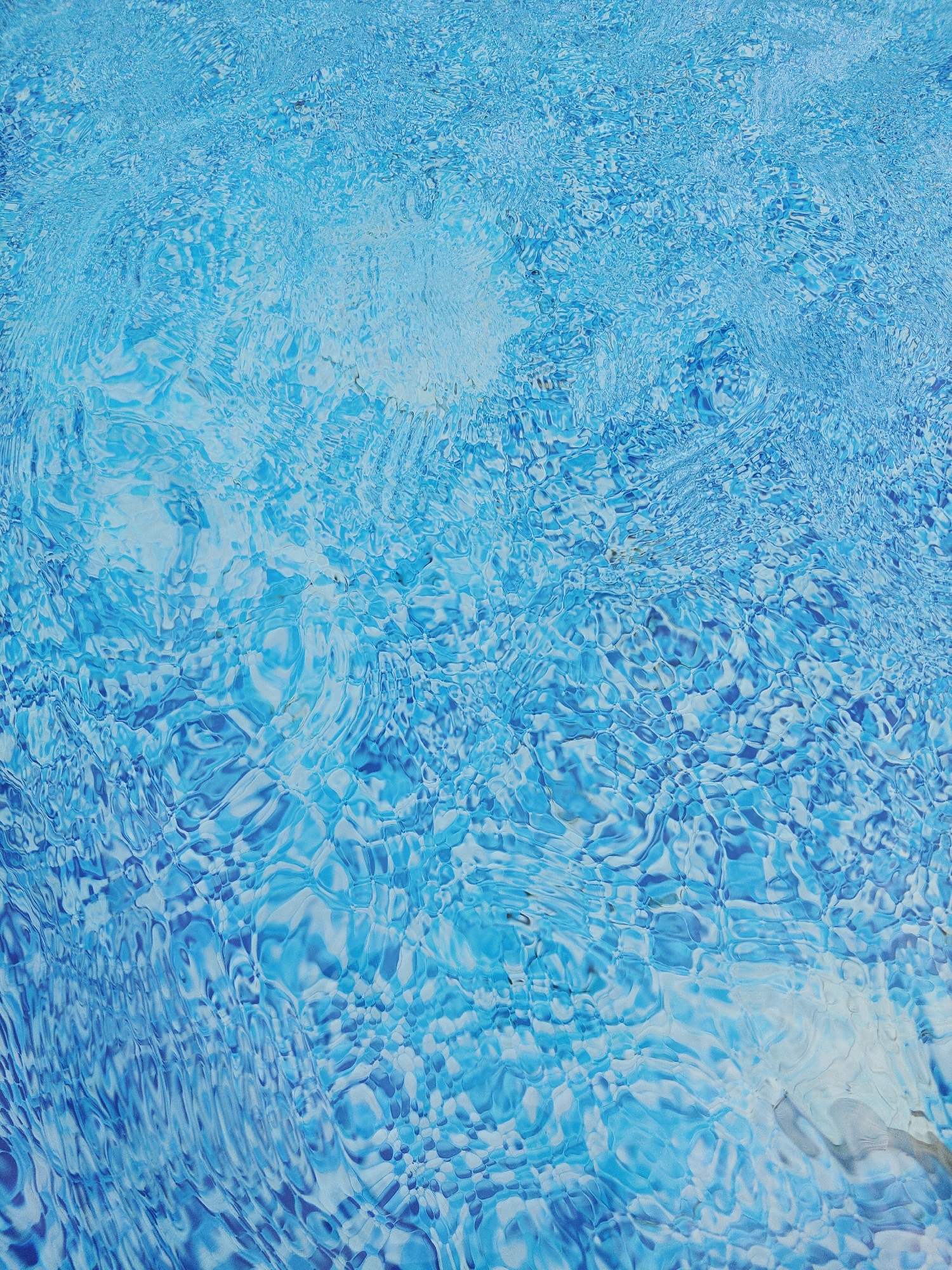 The image shows the surface of a swimming pool with clear, blue water. The water is rippling, creating patterns of light and shadow. There are no people or objects visible in the water. The scene is an abstract view of the water's surface. The image does not contain any information that would allow for identification of its location in the city of Koledino, Russia.