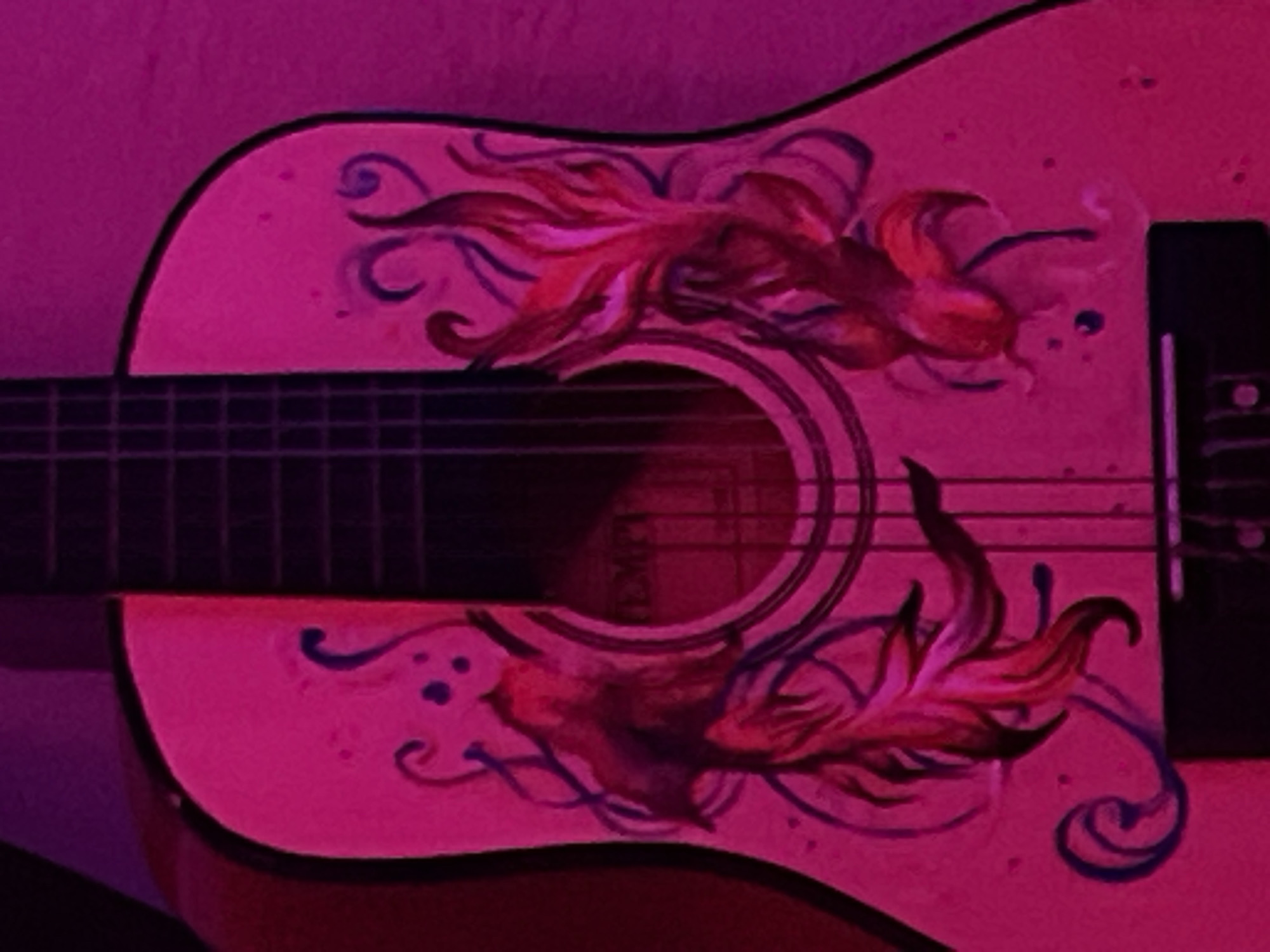 The scene, located in Debelt, Bulgaria, presents a close-up, static shot of the central body of an acoustic guitar, immersed in saturated magenta light. The guitar's surface, likely a light base color, is custom-painted with stylized aquatic motifs. Two prominent figures resembling goldfish or koi, characterized by flowing fins and tails in shades of deep red, orange, and purple, are positioned symmetrically on either side of the central sound hole. These figures are accented with swirling dark blue or indigo lines and scattered small blue dots, suggestive of water or bubbles.
The guitar features a circular sound hole with concentric dark and lighter rings. Indistinct text, possibly "TEMPI," is partially visible on a label within the sound hole. Six metallic strings extend across the sound hole, anchored at a dark bridge visible at the bottom of the frame and leading towards a dark fretboard with discernible frets on the left. No individuals or active interactions are present. The background is uniformly illuminated in magenta, offering no additional environmental details beyond the guitar.