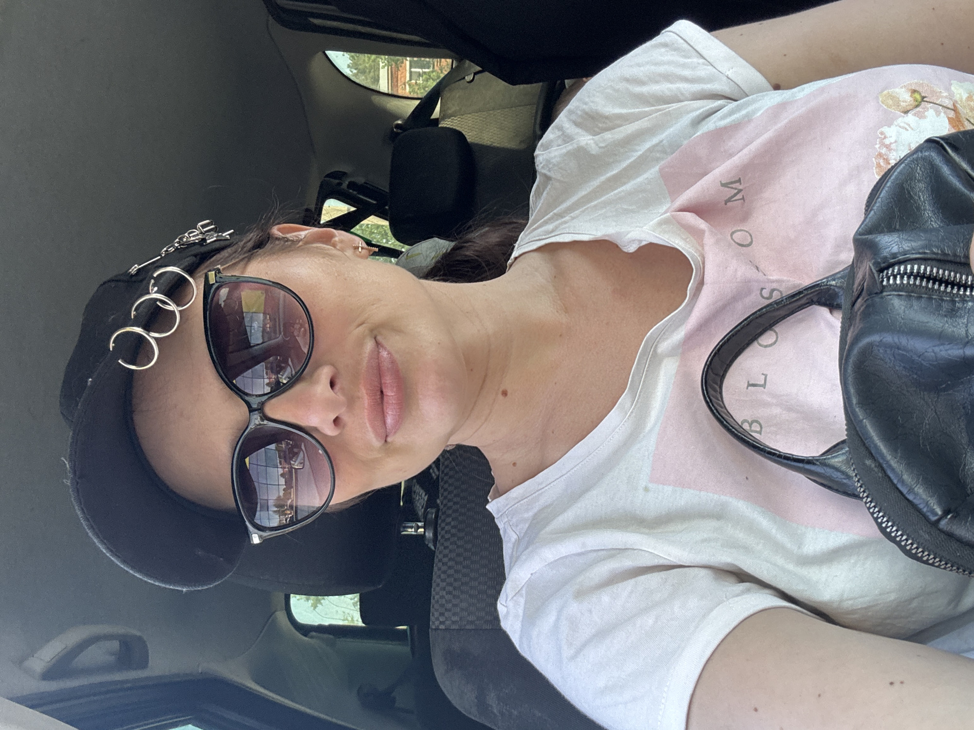 The image shows a woman wearing sunglasses and a black cap in a car. The background includes a window and some blurry outdoor details. Based on the location information, it is likely that the photograph was taken in Chaikovsky, Russia, but the image itself does not provide specific details to confirm this.