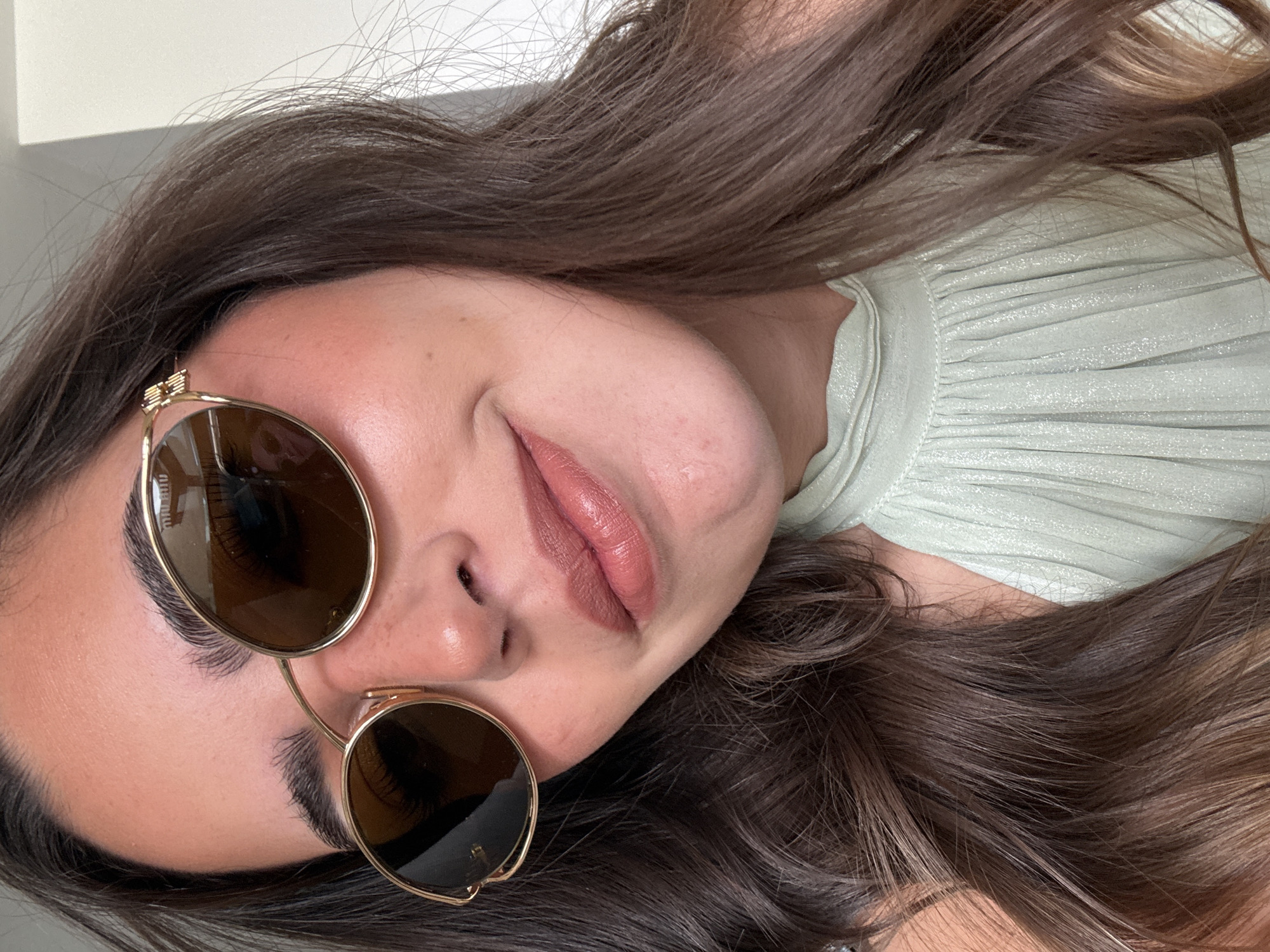 A person with light skin, brown hair, and brown eyes is wearing gold-rimmed sunglasses and light green, pleated clothing. The photo appears to be taken indoors with natural lighting. The location is not discernible as San Bernardino Tlaxcalancingo, Mexico.