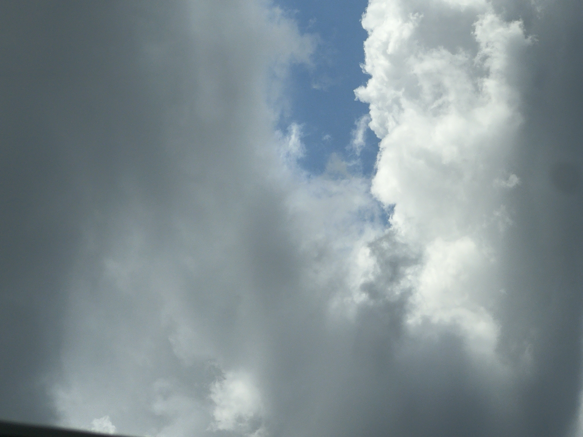 The image is a photograph of the sky, featuring a mix of dark and light clouds. There is a patch of bright blue sky visible between the clouds. The overall impression is of a partly cloudy day. The image does not contain any recognizable landmarks or features that would allow for identification of a specific location, including Warsaw, Poland. There are no people, subjects, objects, or actions depicted in the image.