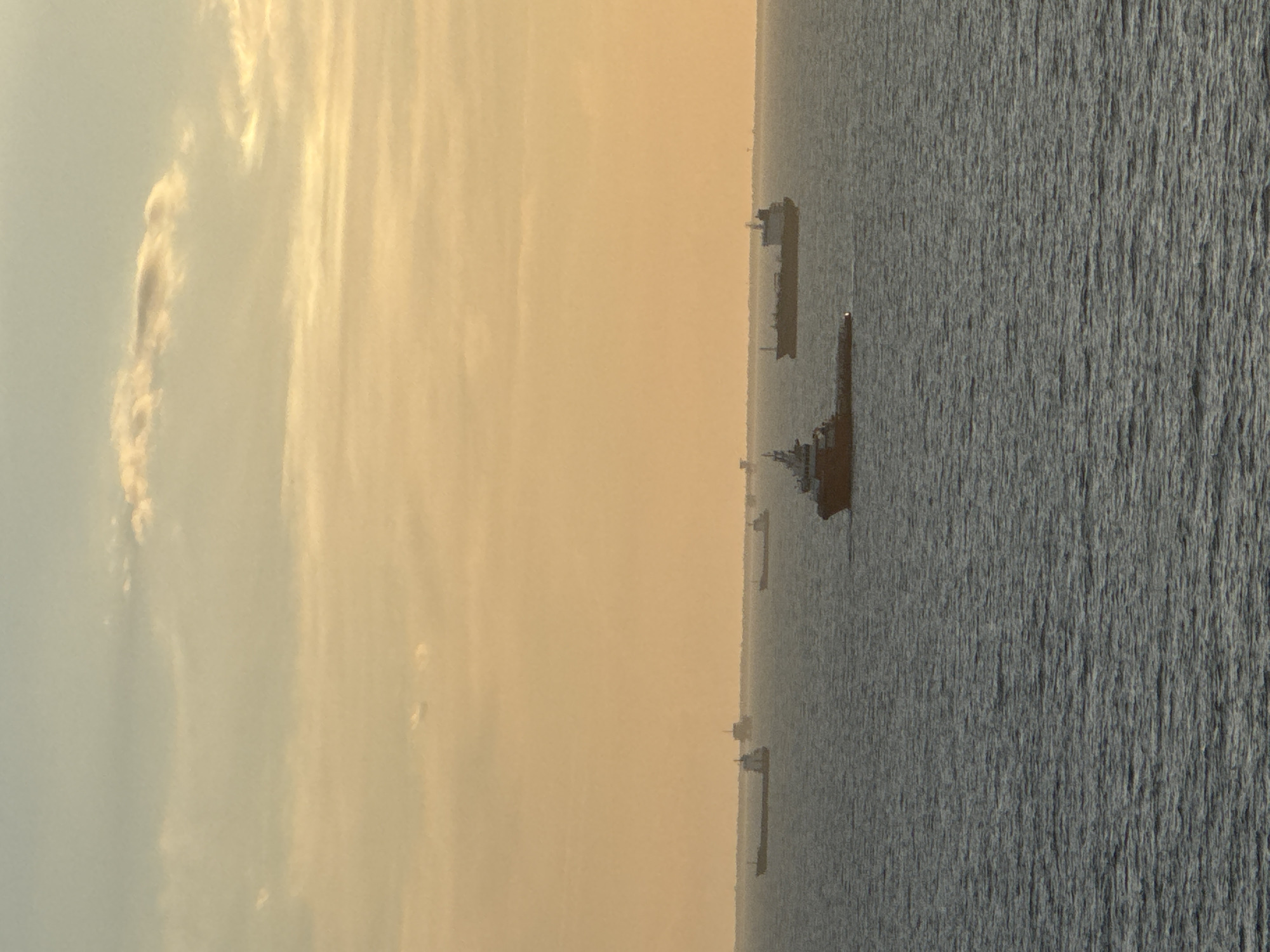 The image depicts several ships at sea off the coast of an unidentified location, possibly near Unknown, Italy. The sky is filled with clouds and appears to be during either sunset or sunrise, indicated by the colors of the sky. The sea is dark and textured. Multiple ships of varying sizes are visible in a line.