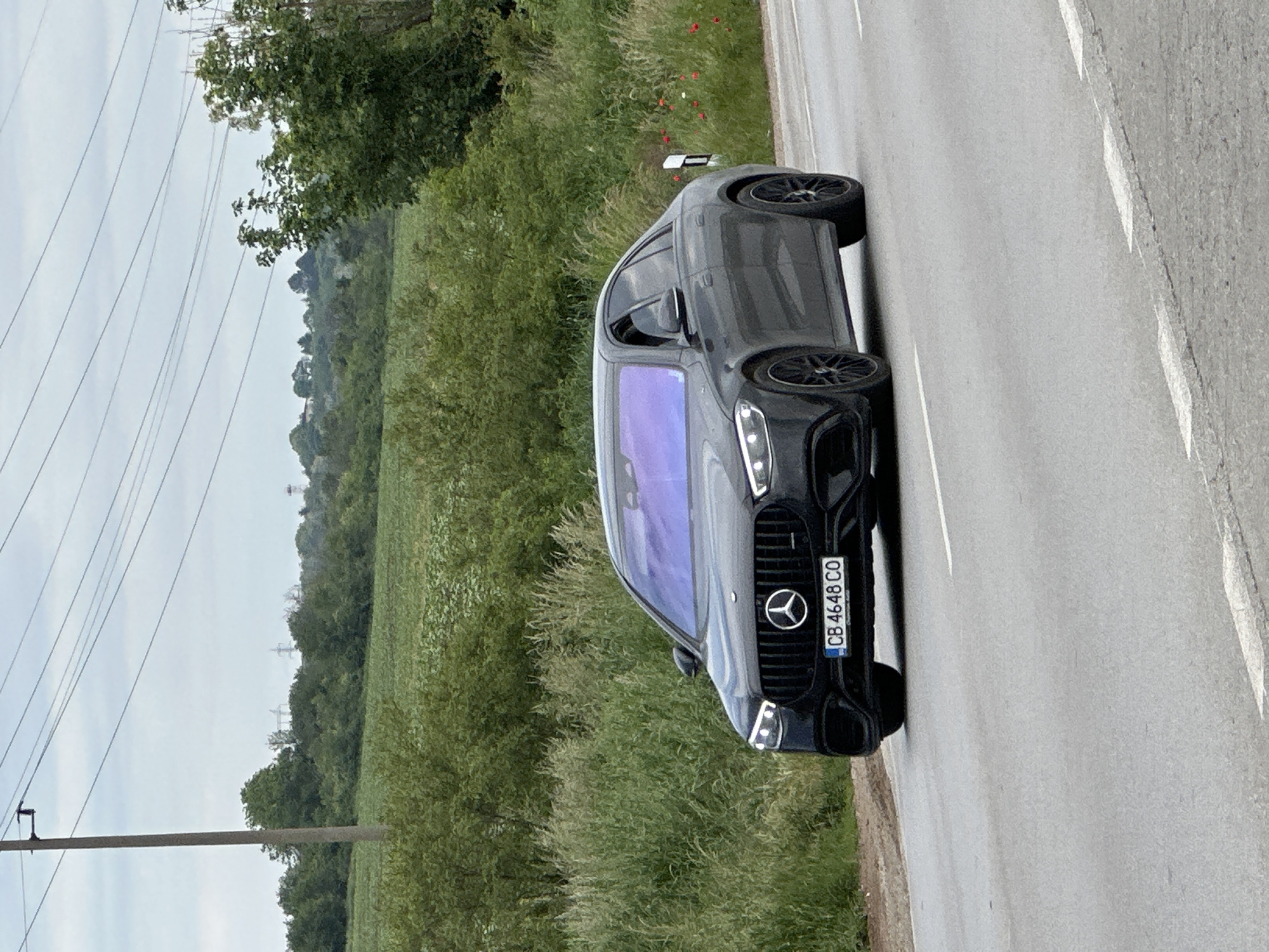 The image shows a black Mercedes-Benz SUV parked on the side of a road. The license plate reads "CB 4648 CO." The background consists of grassy fields and trees, characteristic of a rural setting. Power lines are visible in the sky. The picture may have been taken in or near Ledenik, Bulgaria, judging from the license plate code "CB" indicating the Veliko Tarnovo Province.