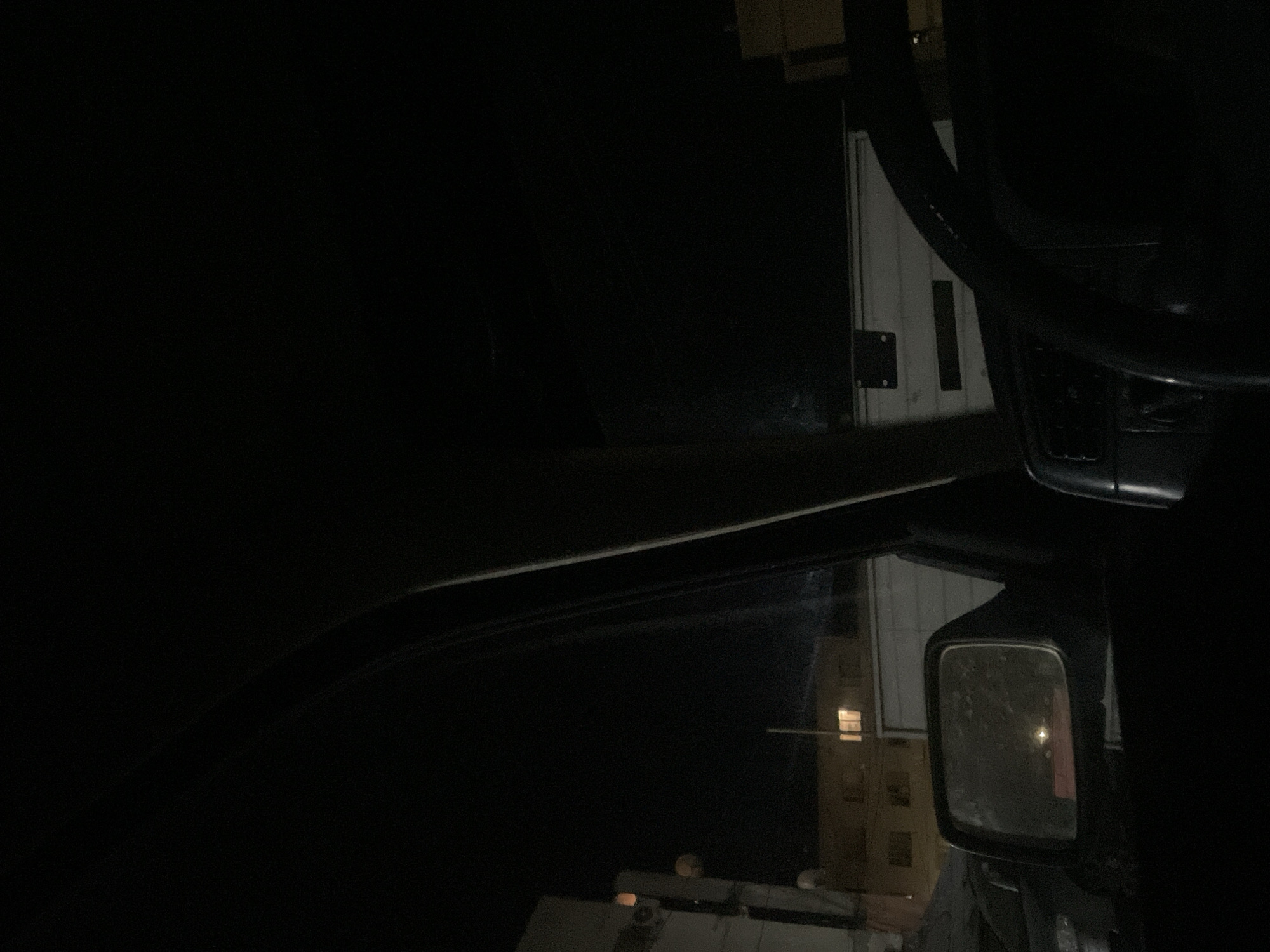 The image is taken from inside a vehicle at night. A steering wheel is partially visible in the top right. The side mirror reflects a building with a lighted window. The location is likely Debelt, Bulgaria.