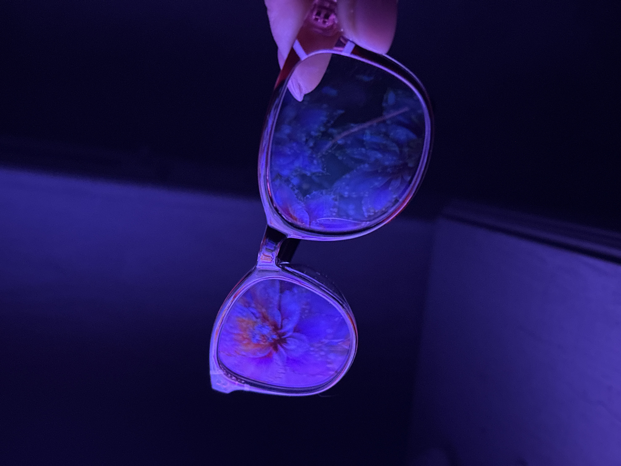 A pair of glasses is held up, reflecting a scene with flowers. The entire image has a strong blue tint. It is impossible to determine the specific location in Chaikovsky, Russia, or the exact nature of the reflected scene without further information.
