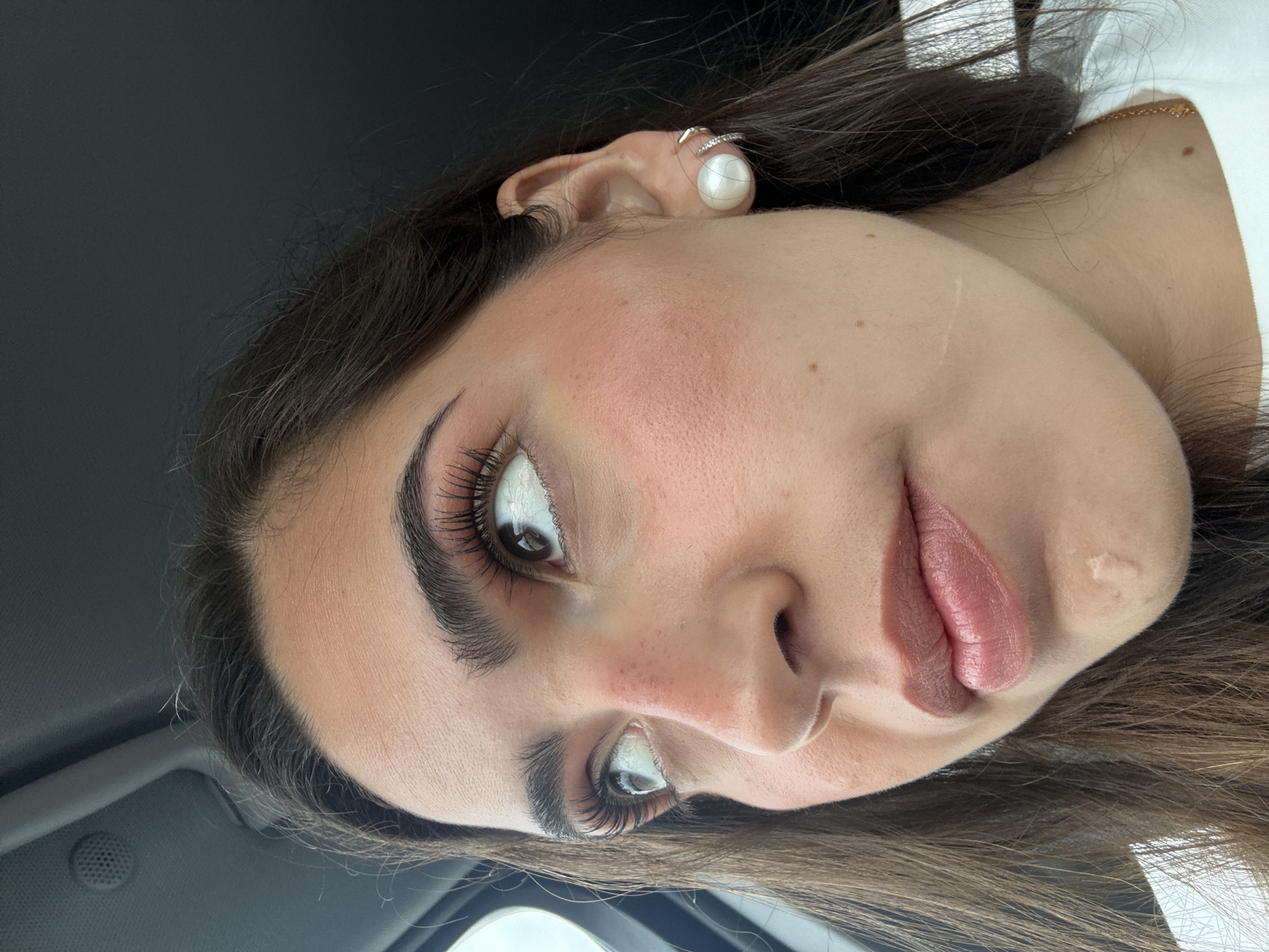 A close-up, slightly rotated image shows a person's face. The individual has brown hair and light skin. They are wearing makeup, including blush, lipstick, and well-defined eyebrows with prominent eyelashes. The person is wearing a pearl earring.
Due to the lack of contextual clues within the image, a specific location in San Antonio cannot be determined.