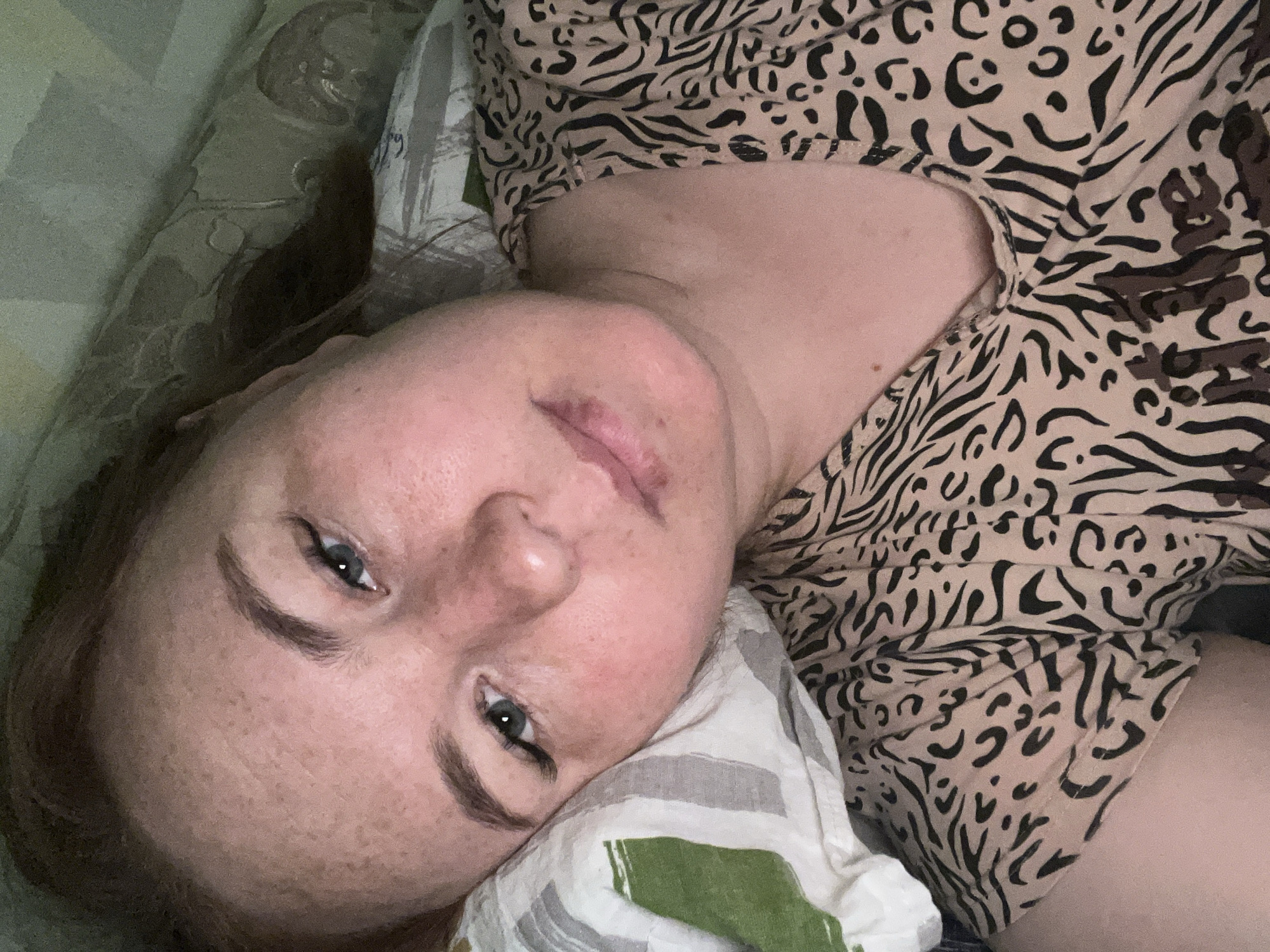 A woman lies on a pillow, wearing an animal print top. The location is not discernible from the image.
