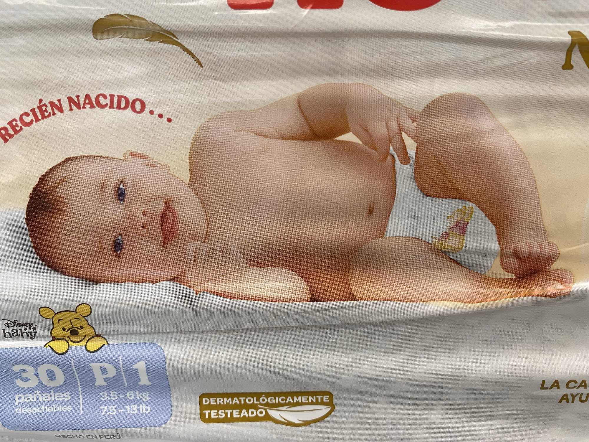 The image shows a close-up of a diaper package. The packaging features a photograph of a baby wearing a diaper with Winnie the Pooh. The package also contains the words "RECIÉN NACIDO" and includes information such as "30 pañales desechables" and weight measurements in kilograms and pounds (3.5-6 kg, 7.5-13 lb). The logo "Disney Baby" and the phrase "DERMATOLÓGICAMENTE TESTEADO" are visible. The text "HECHO EN PERÚ" indicates the country of origin. There is no indication of the city of Tinaquillo, Venezuela in the image.